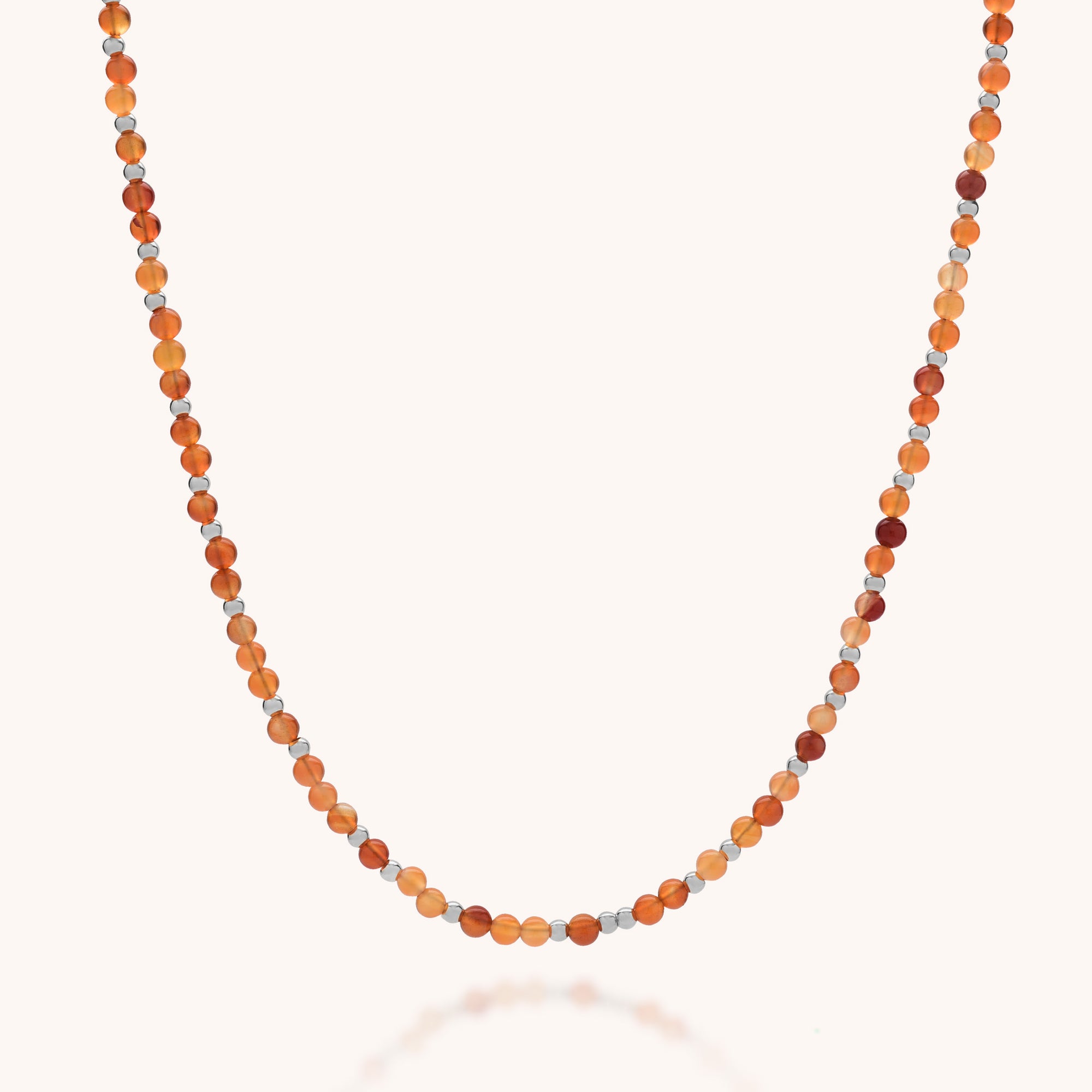 The Jewel Bead Birthstone Necklace - July features small round Carnelian beads in orange, brown, and light beige, evenly spaced on eco-friendly sterling silver in a single strand displayed on a light background.