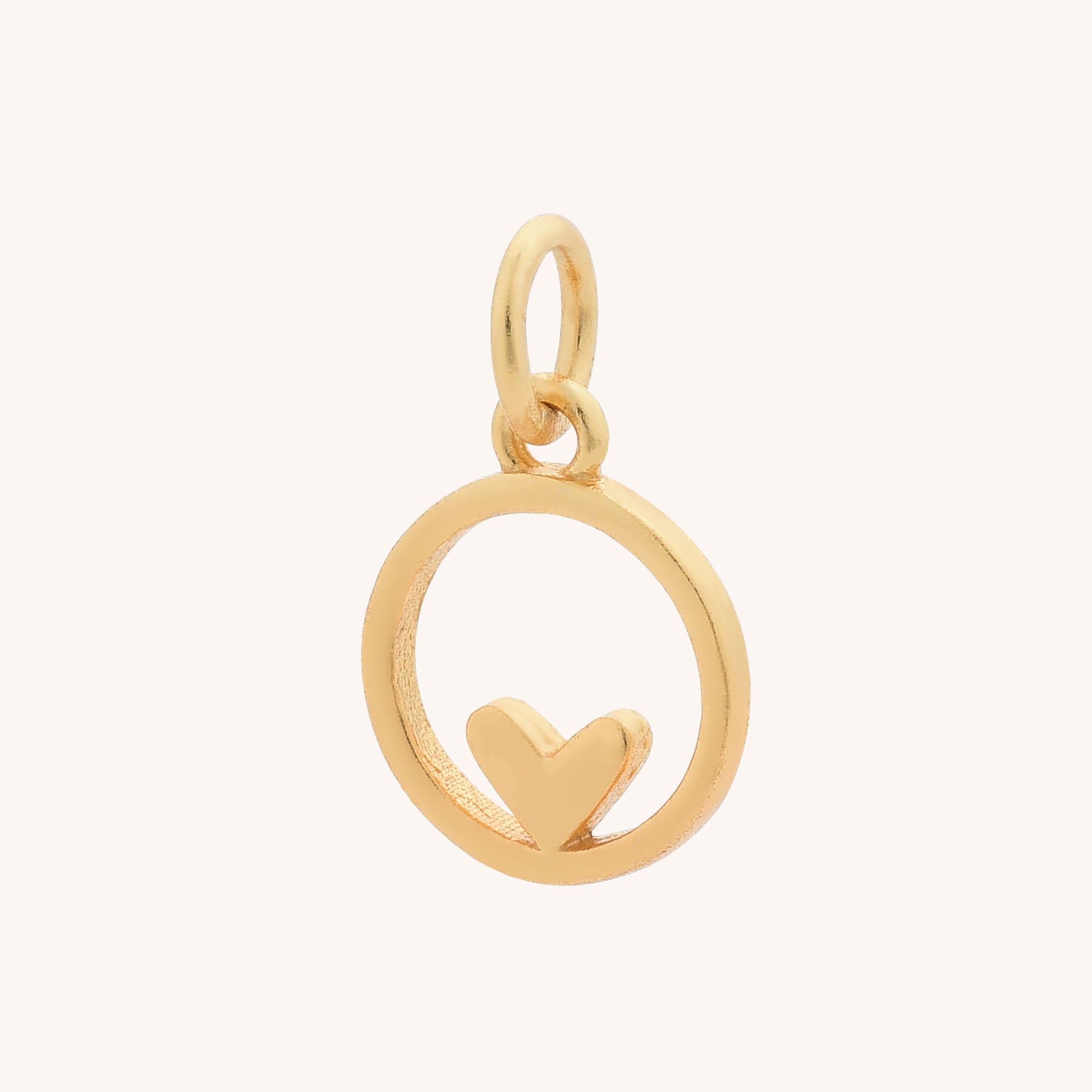 The Circular Heart Charm features a circular frame with a small heart at the bottom and a loop for attaching to a chain, making it a delicate addition to any jewellery collection. Shown against a plain light background.
