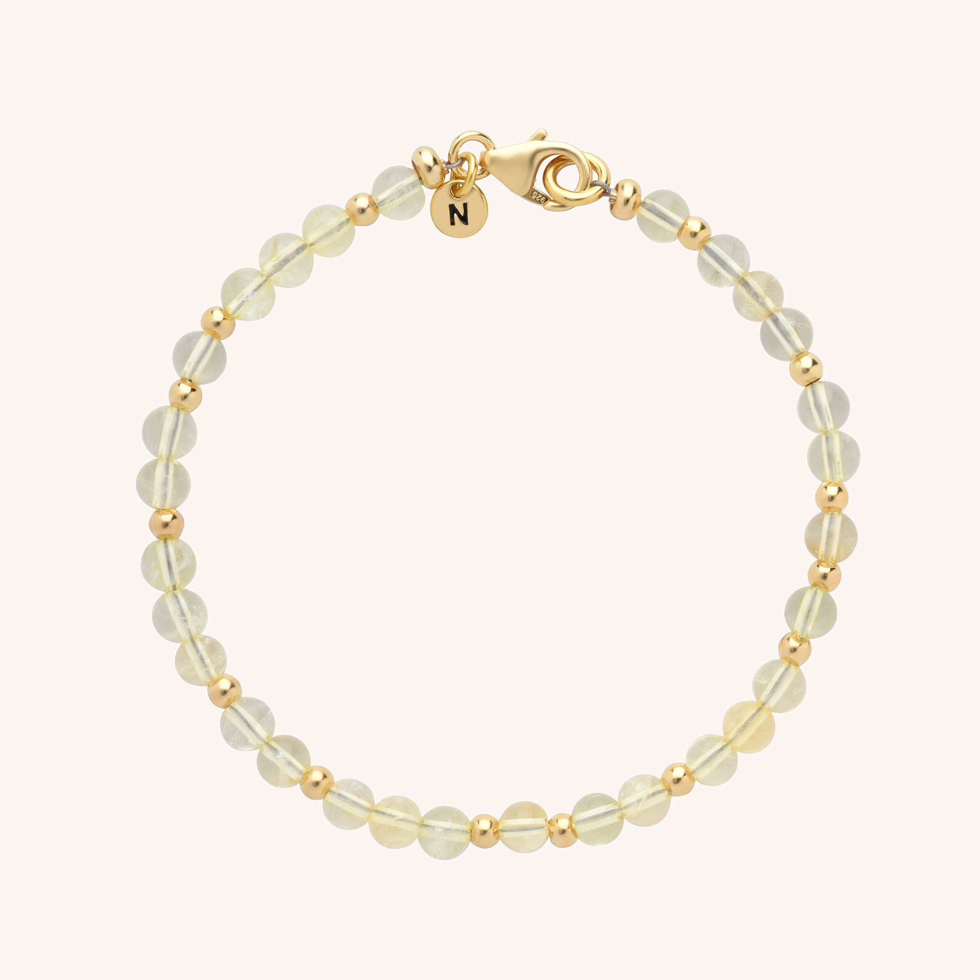 The Jewel Bead Birthstone Bracelet features alternating round translucent beads and small gold beads, finished with a gold clasp and a round charm engraved with the letter N.
