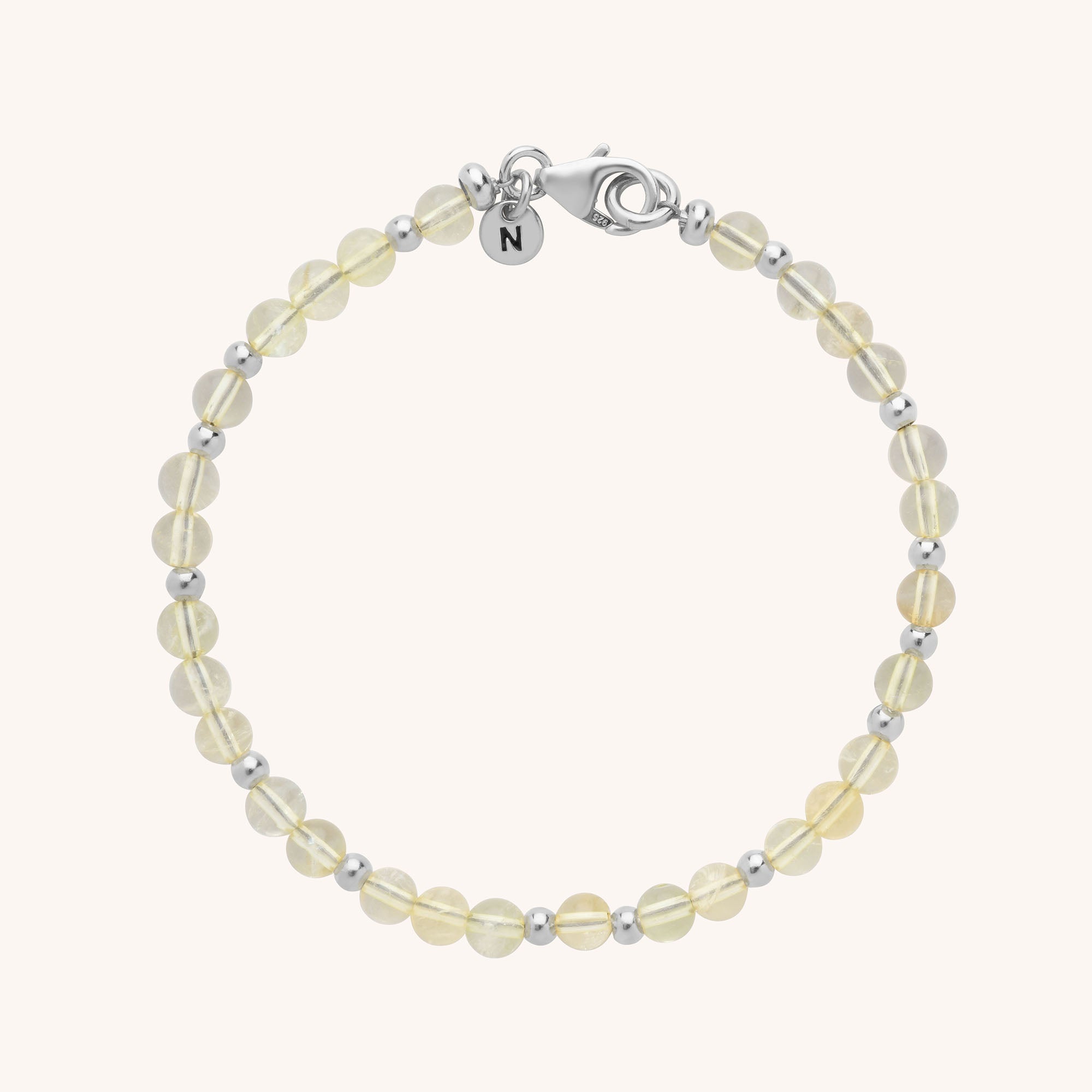 The Jewel Bead Birthstone Bracelet features round, pale yellow beads alternated with silver beads, finished with a silver lobster clasp and a charm engraved with N—a beautiful piece of handmade jewellery.
