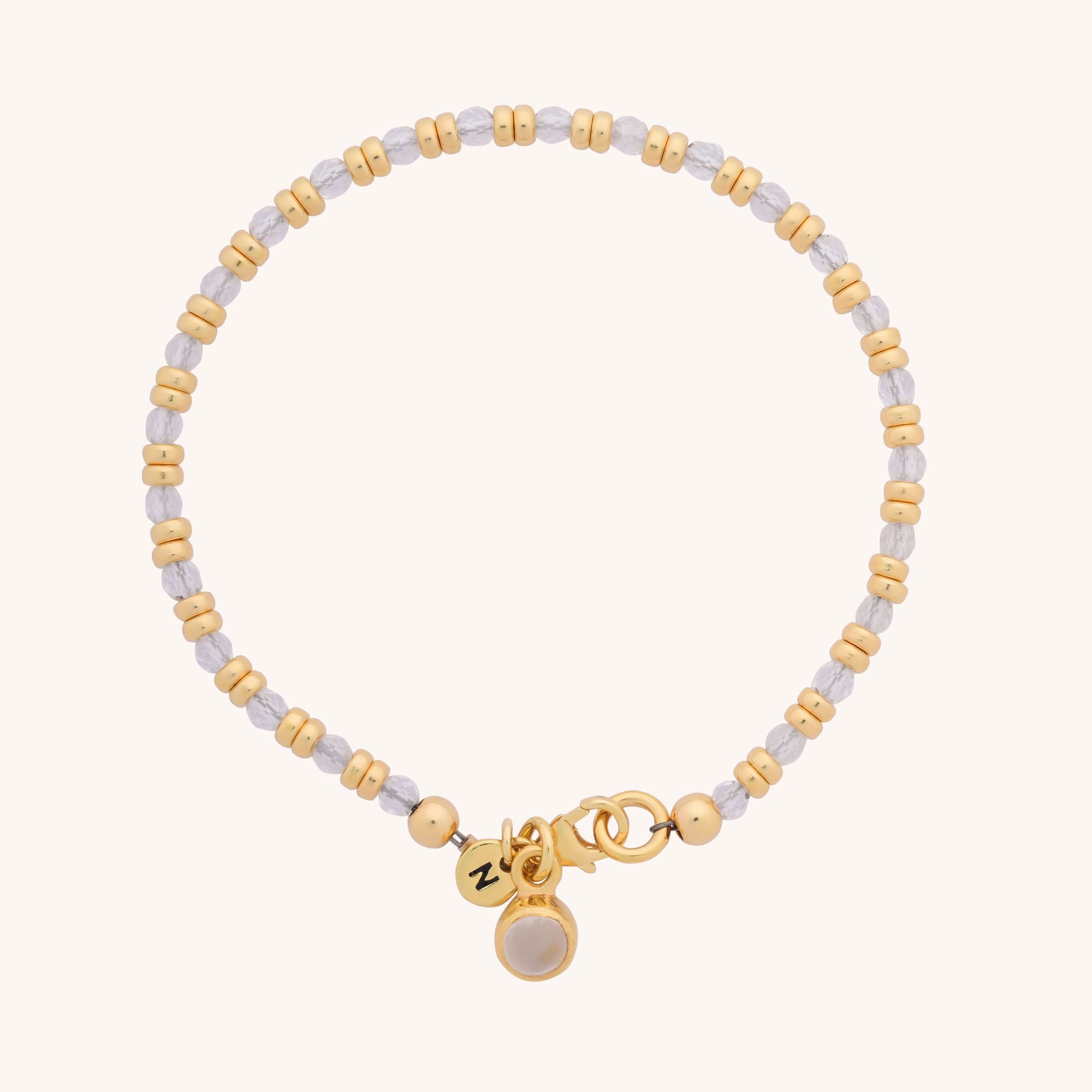 The Linear Birthstone Bracelet features alternating gold and silver beads, a gold clasp, and two small gold charms—one round with an engraving and the other adorned with a white birthstone—ideal for gemstone jewellery lovers.