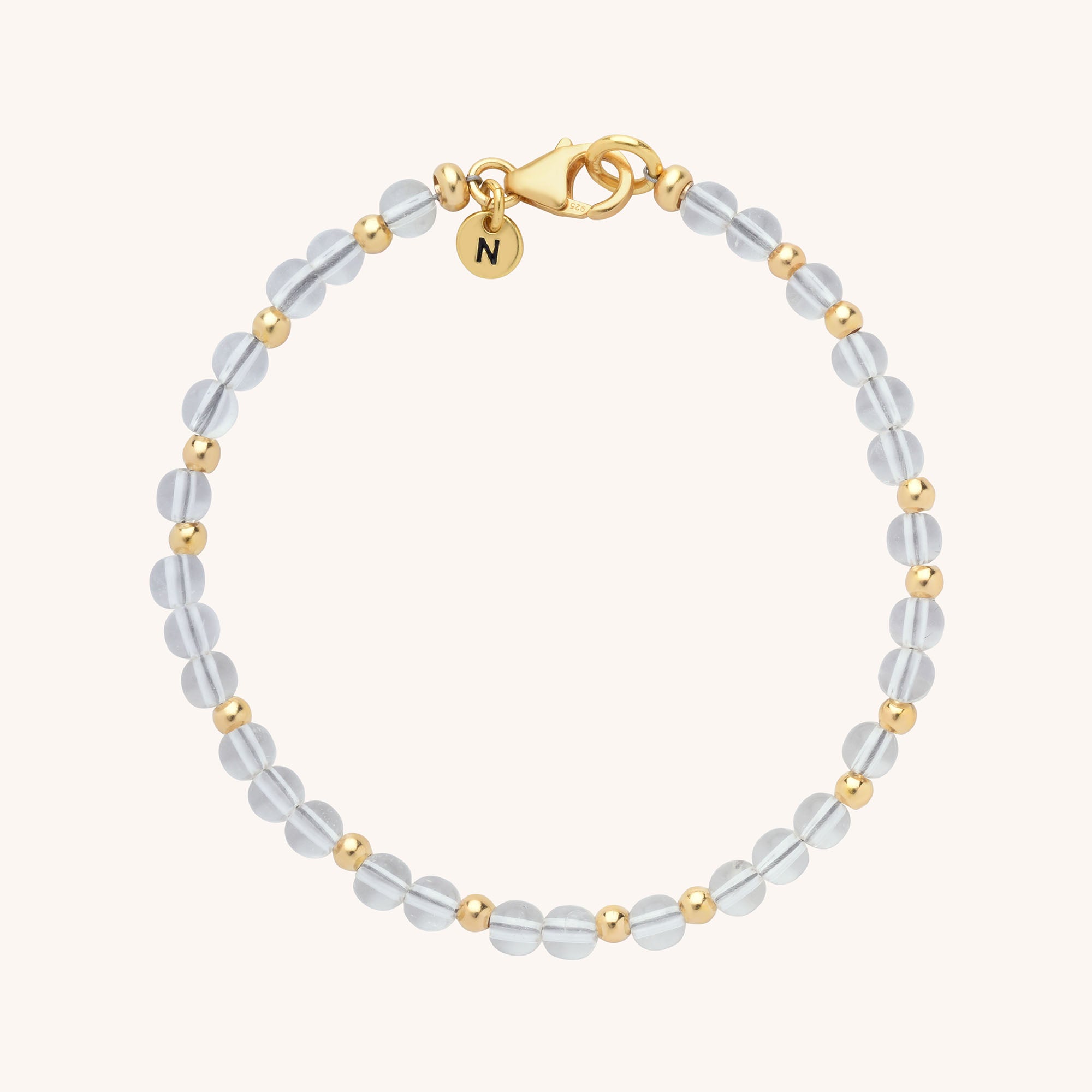 The Jewel Bead Birthstone Bracelet features alternating translucent round beads and small gold beads, with a gold clasp and a round gold charm engraved with the letter N.