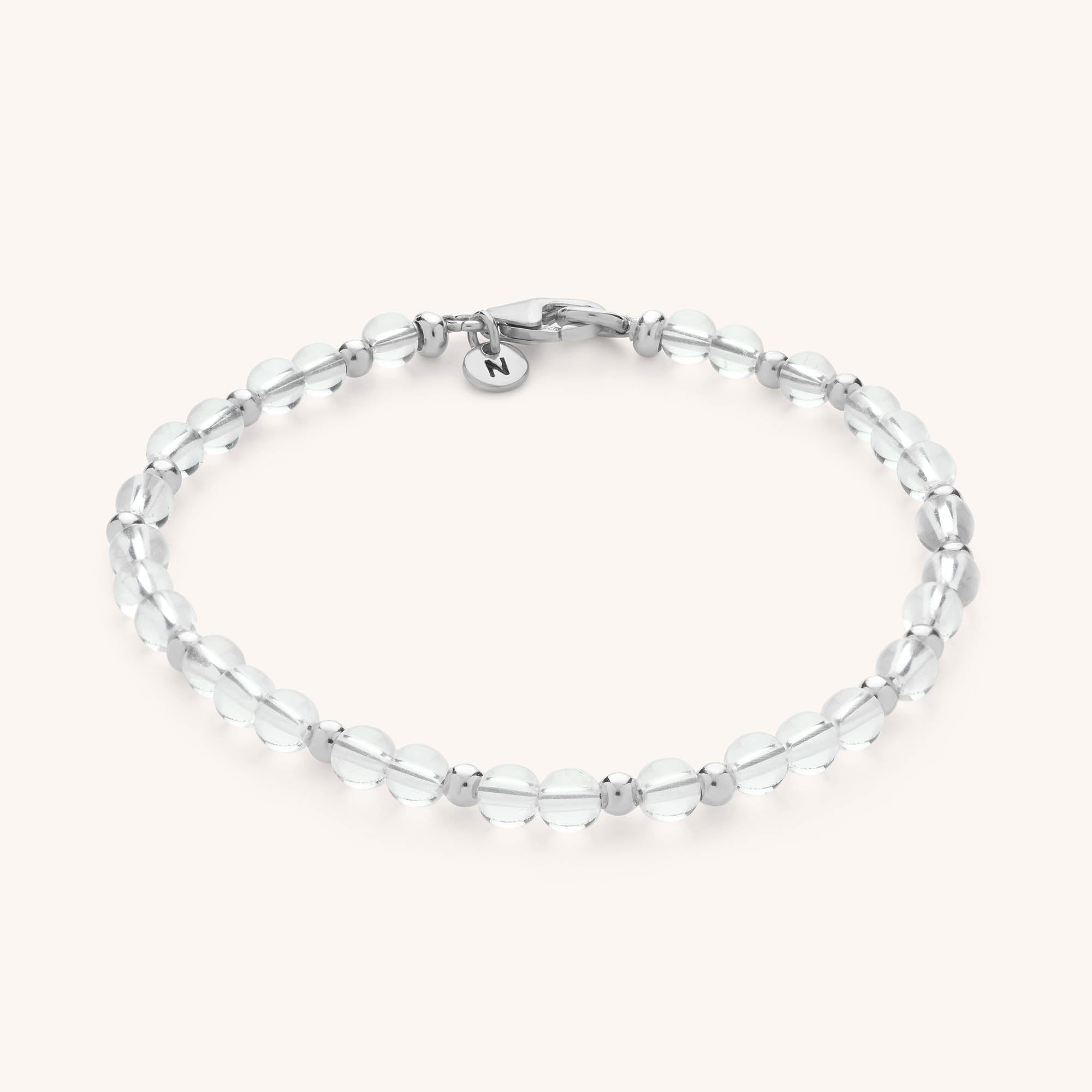 A delicate handmade jewellery piece, the Jewel Bead Birthstone Bracelet features clear round beads, silver spacers, a silver clasp, and a small round charm engraved with the letter N.