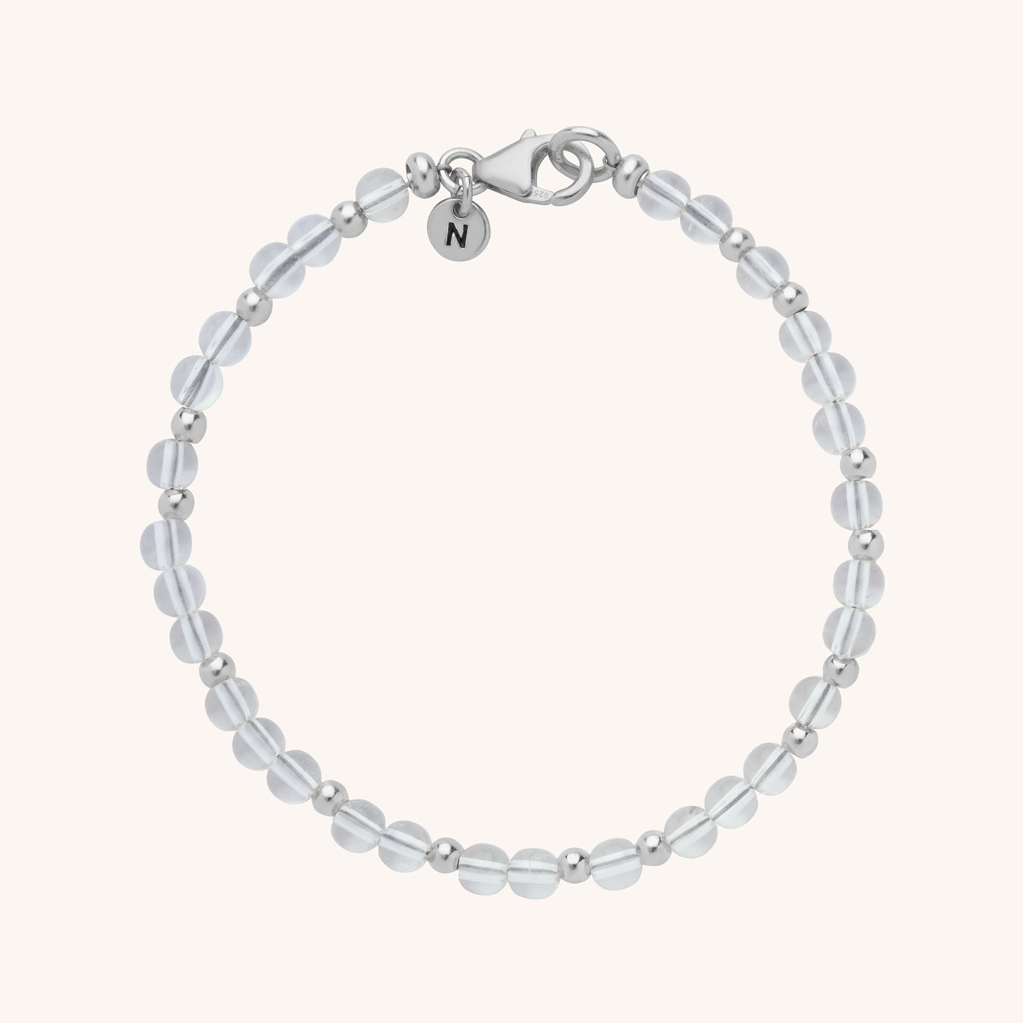 The Jewel Bead Birthstone Bracelet features alternating round translucent beads and small silver beads, finished with a silver lobster clasp and a circular charm engraved with the letter N—a perfect handmade piece.