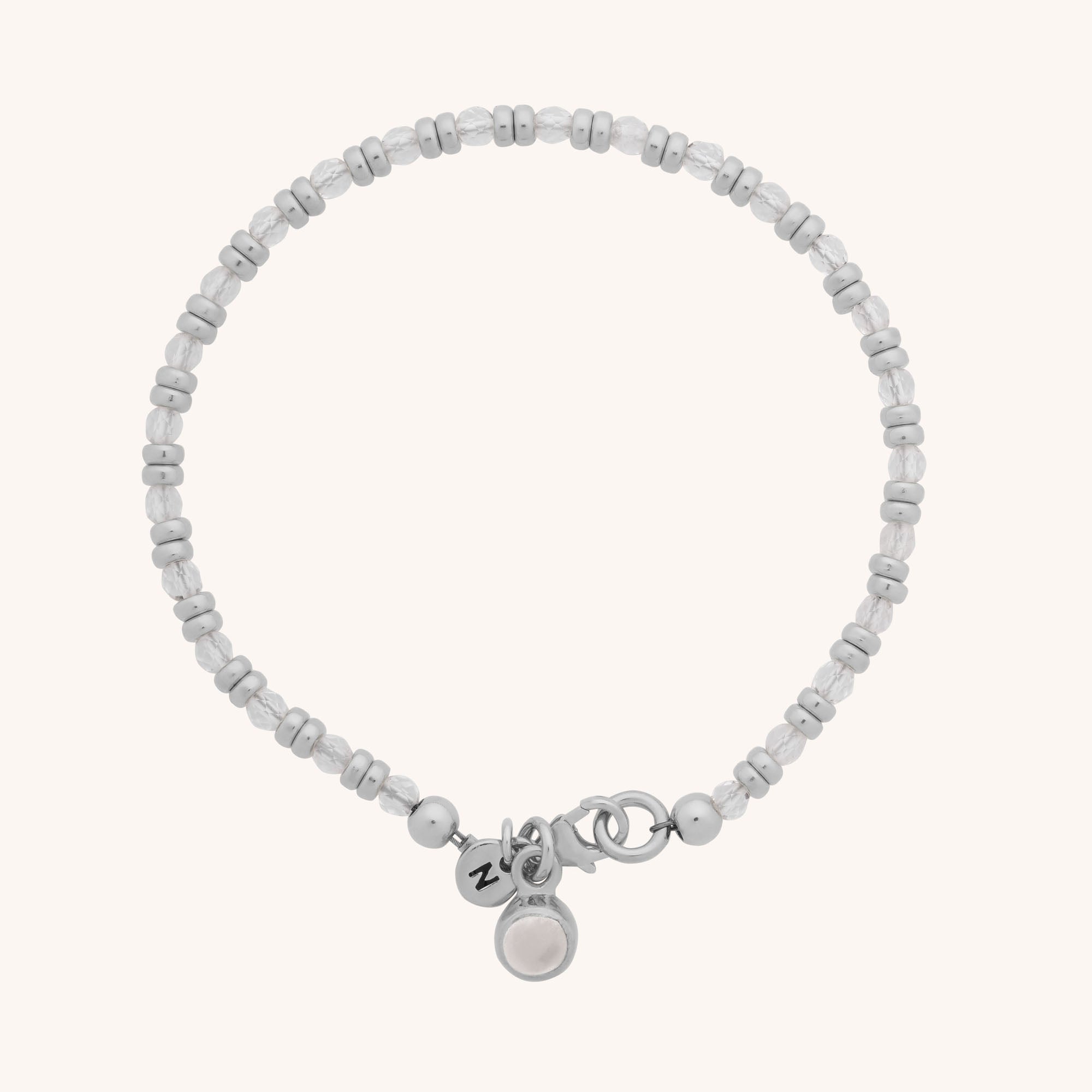 The Linear Birthstone Bracelet is a delicate silver beaded bracelet with round and barrel beads, featuring two charms: a disc engraved with NZ and another with a white natural gemstone—ideal for gemstone jewellery lovers.