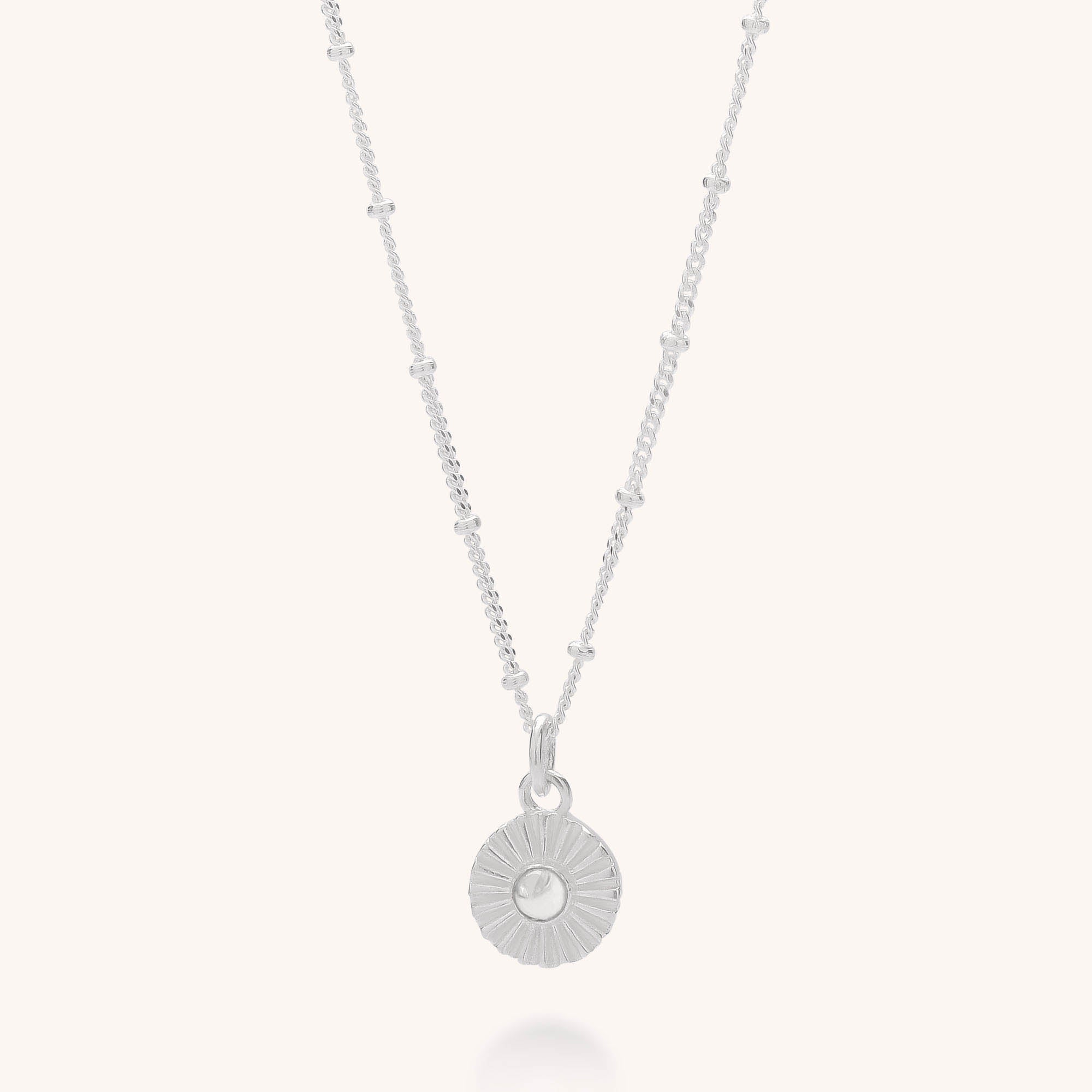 The Radiance Birthstone Necklace - April features a sterling silver textured circular pendant and a delicate chain with evenly spaced bead accents, shown on a plain white background.