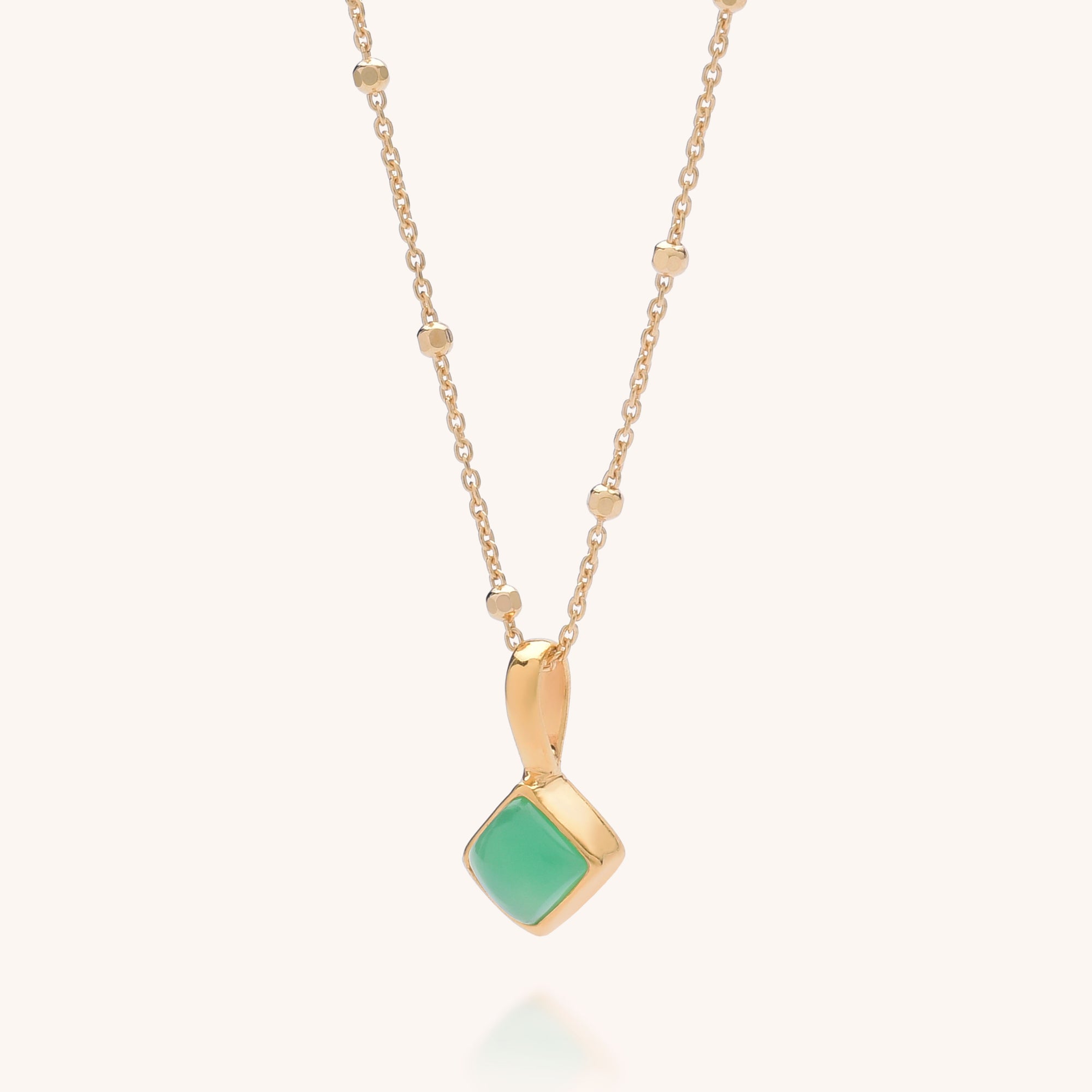 The Diamond Birthstone Necklace May features a delicate gold chain with small gold beads and a pendant set with a square green Chrysoprase stone framed in gold, believed to hold healing properties.