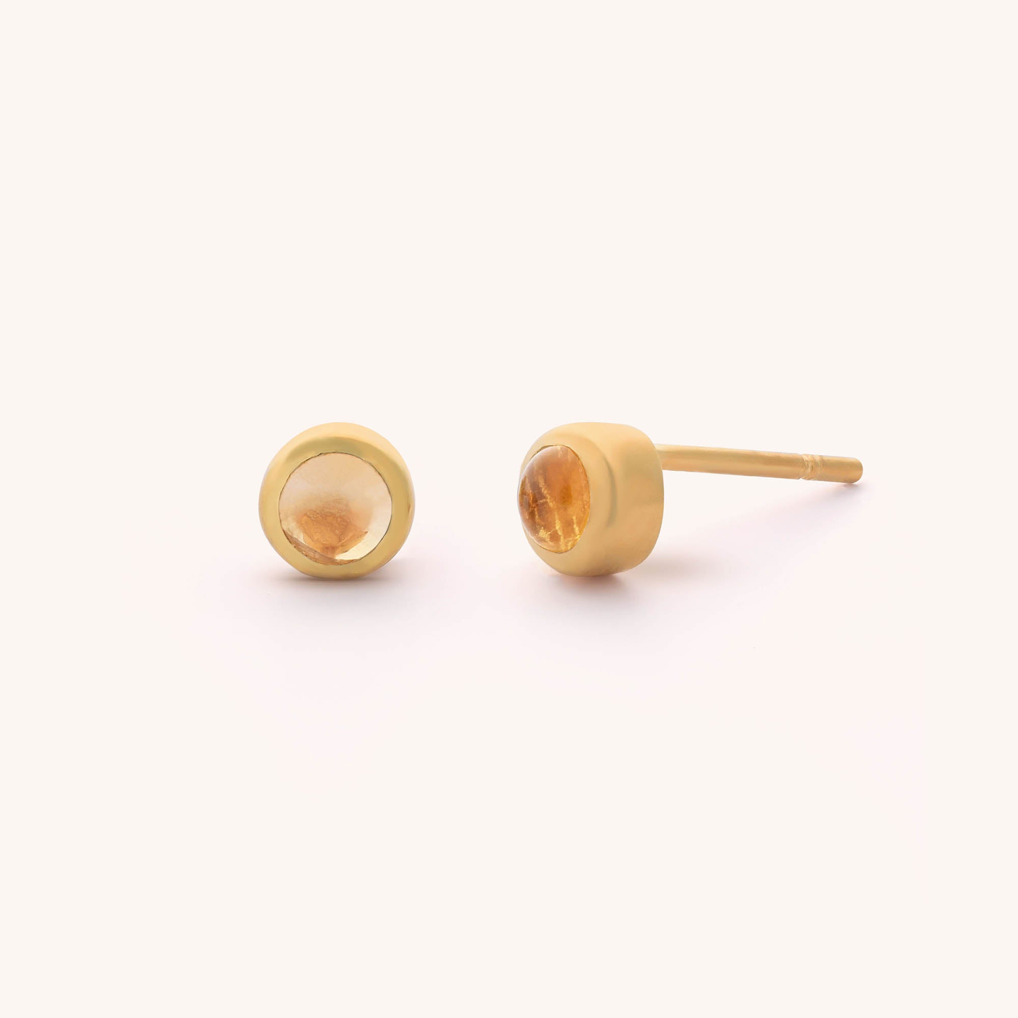 The Mini Gem Dot Birthstone Earrings - November feature two gold stud earrings with round citrine gemstones, the timeless November birthstone, set in a smooth bezel and displayed on a plain, light background.