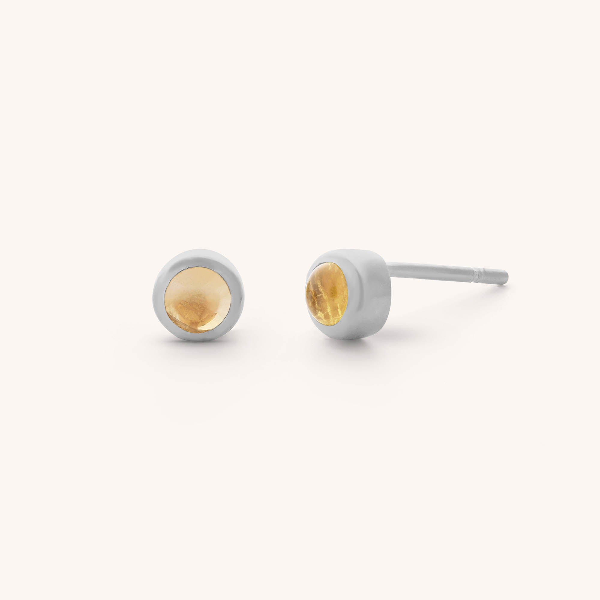 Discover our Mini Gem Dot Birthstone Earrings - November: round citrine gemstones are set in sleek silver bezels, creating elegant stud earrings. The warm, yellow-orange hue of the citrine stands out beautifully against a soft, off-white background.