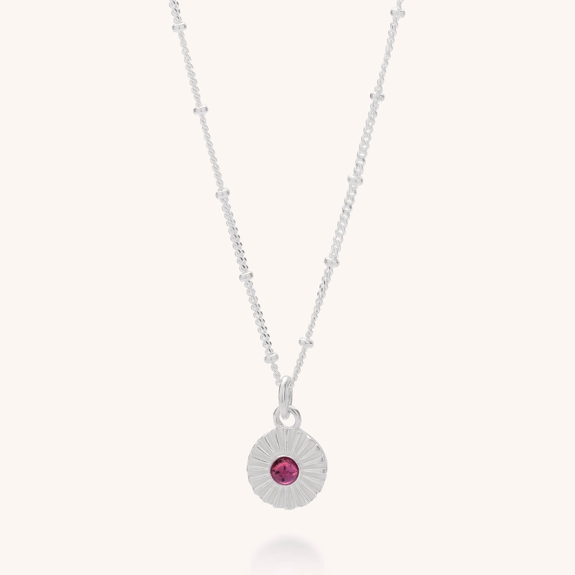 The Radiance Birthstone Necklace - January features a sterling silver chain with small round beads, a textured circular pendant, and a central garnet gemstone—making it an ideal birthstone necklace.