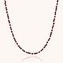 The Jewel Bead Birthstone Necklace - January features handmade alternating small round gold and deep red garnet beads in a simple, elegant pattern against a light background.