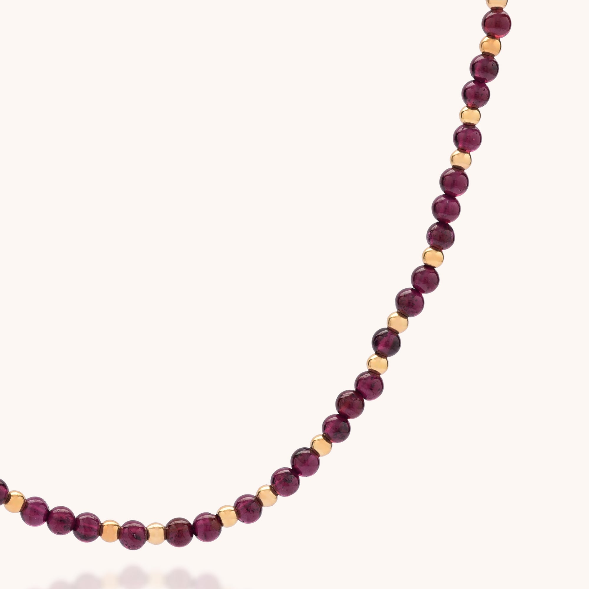 A close-up of the Jewel Bead Birthstone Necklace - January, handmade with alternating small gold and round deep red garnet beads, displayed on a light background.