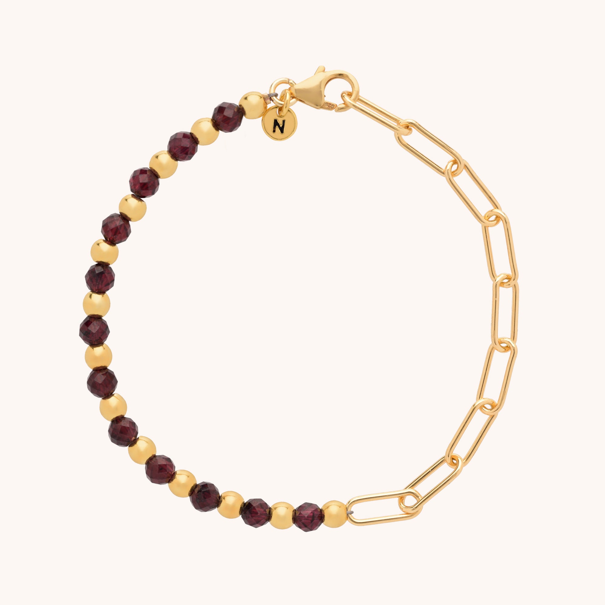 The Gem Shine Bracelet features half gold chain links and half alternating gold and dark red gemstones, finished with a small round N-engraved charm near the clasp.