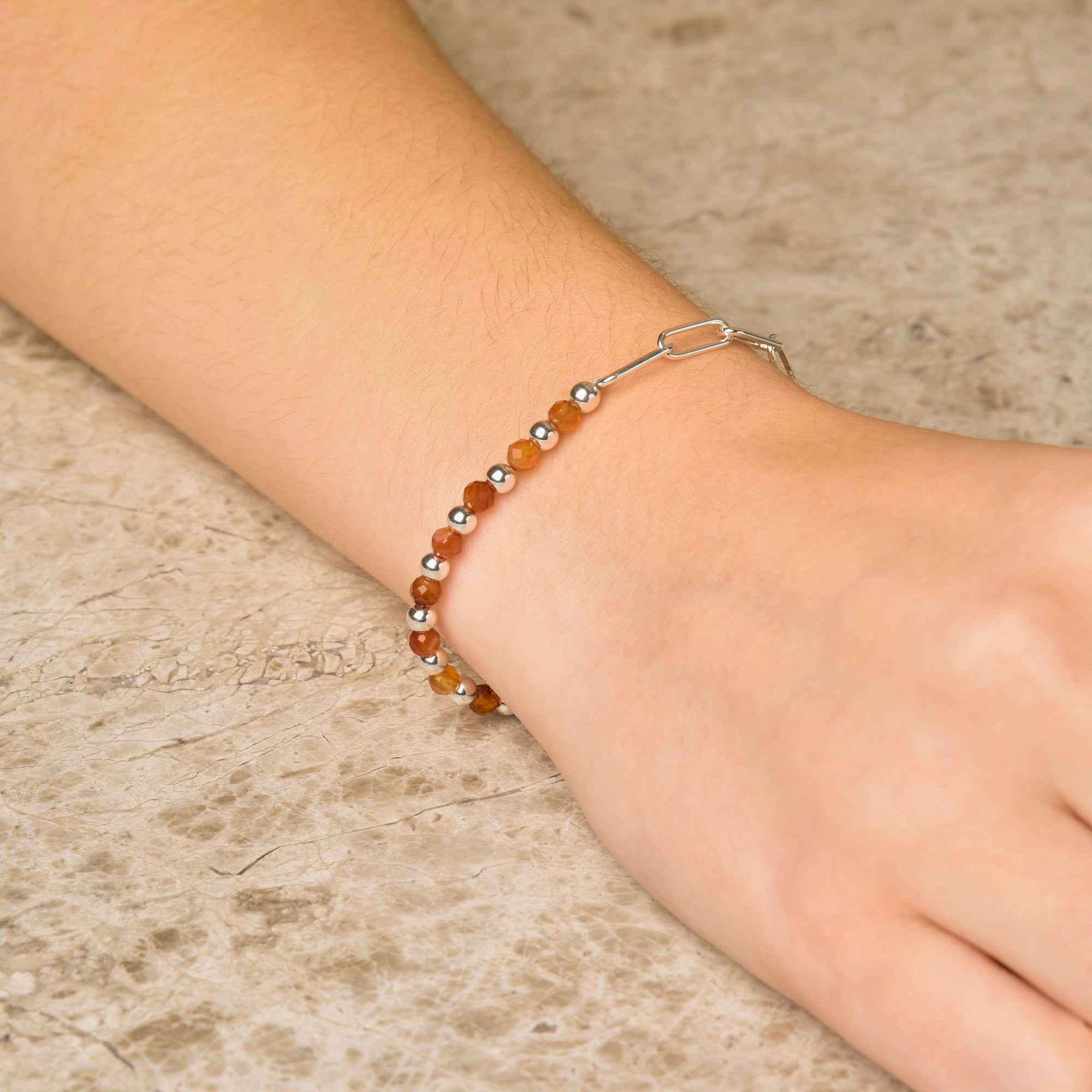 A close-up of a wrist wearing the Gem Shine Bracelet, with brown natural gemstones and eco-silver beads, resting on a light stone surface.