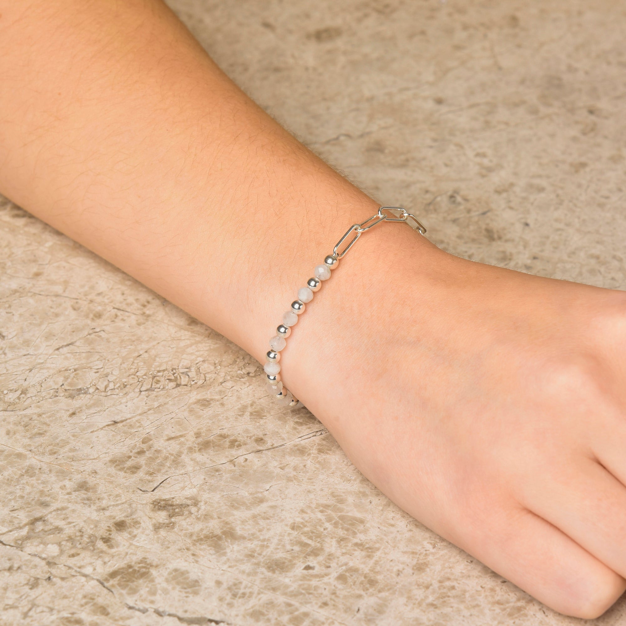 A close-up of a wrist wearing the Gem Shine Bracelet, made from eco-silver sterling silver with small round beads, showcased on a light textured stone surface.