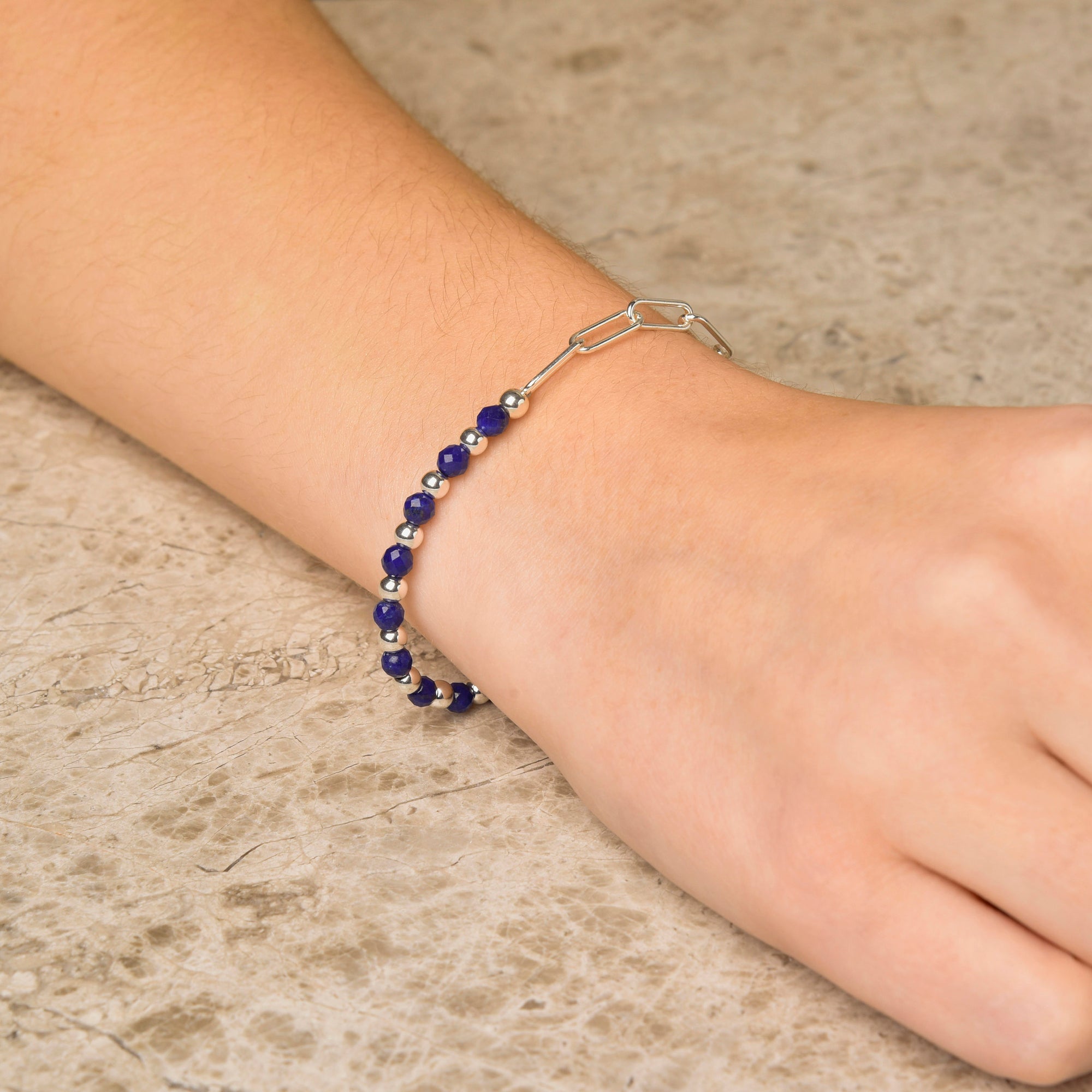 A close-up shows the Gem Shine Bracelet on a wrist, with round blue natural gemstones and eco-silver sterling silver accents, displayed on a light beige textured surface.