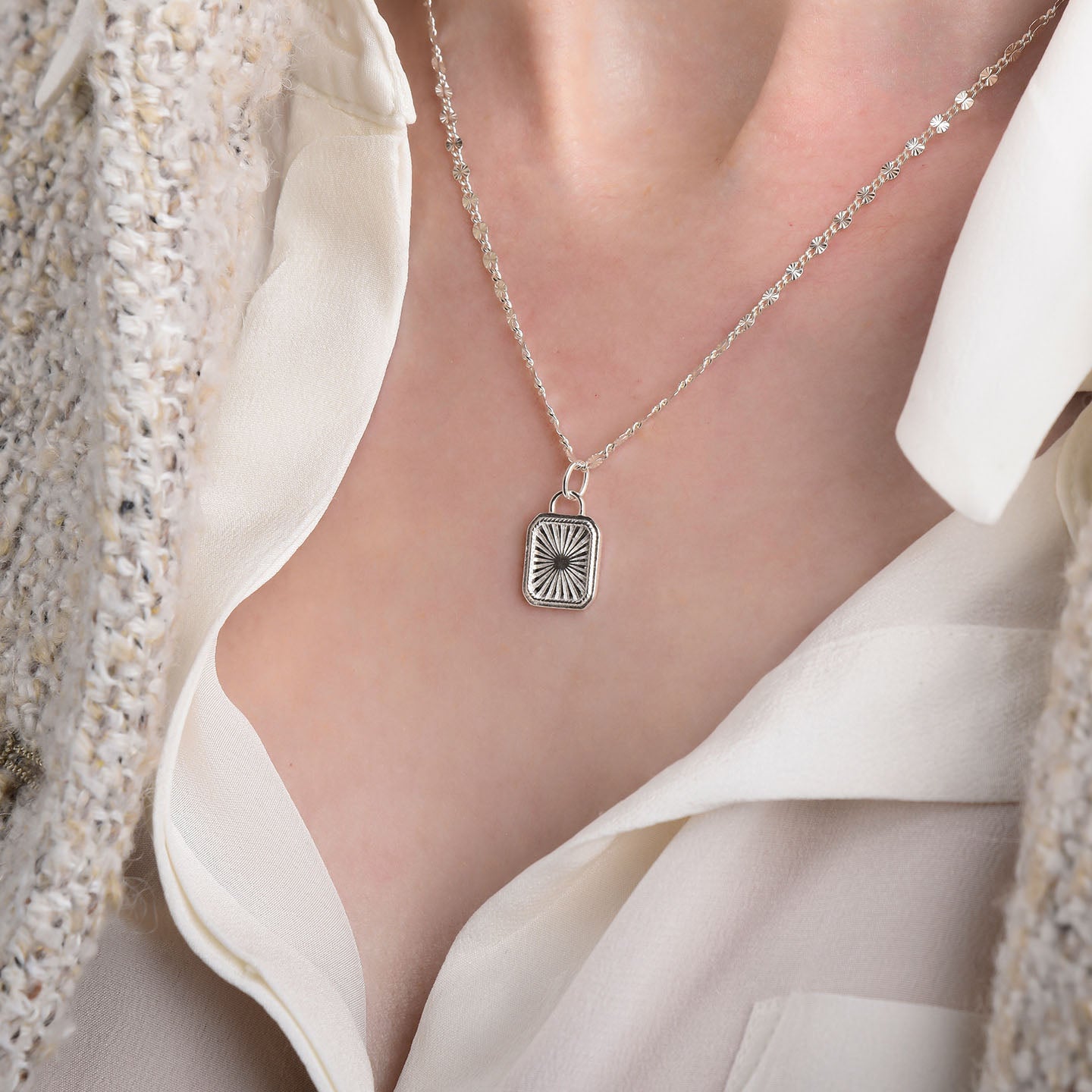 A close-up shows the Golden Dawn Necklace—a textured sterling silver sunburst pendant—worn over a cream blouse and light tweed jacket.