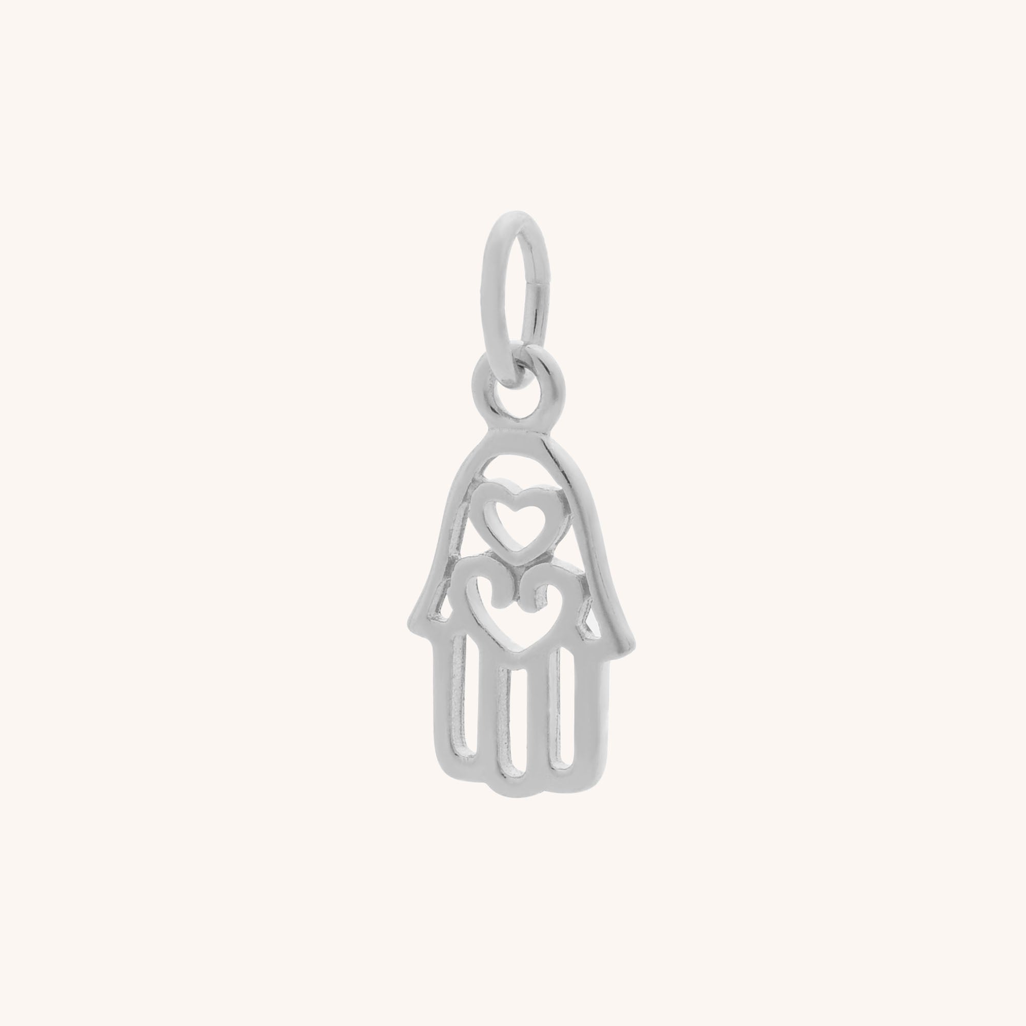 The Hamsa Hand Charm is crafted in sterling silver with an open design, showcasing two heart shapes—one on the palm and one at the center. A small top loop makes it easy to attach to your favorite necklace or bracelet.