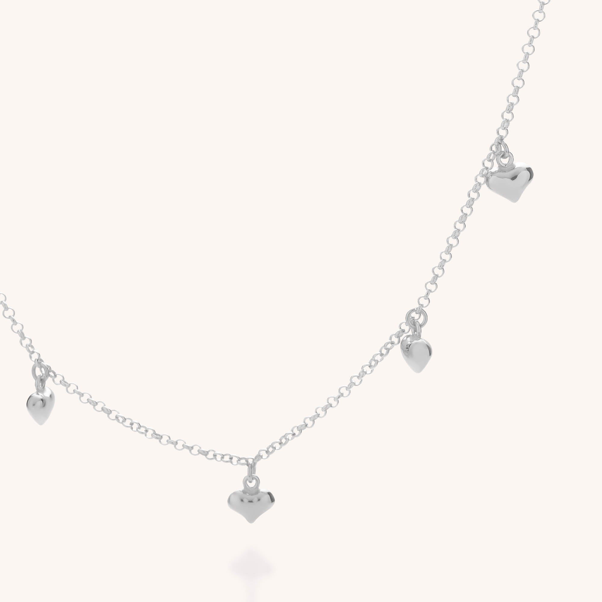 The Floating Heart Charm Necklace features four shiny, heart-shaped pendants on an eco sterling silver chain, beautifully displayed on a light, neutral background.
