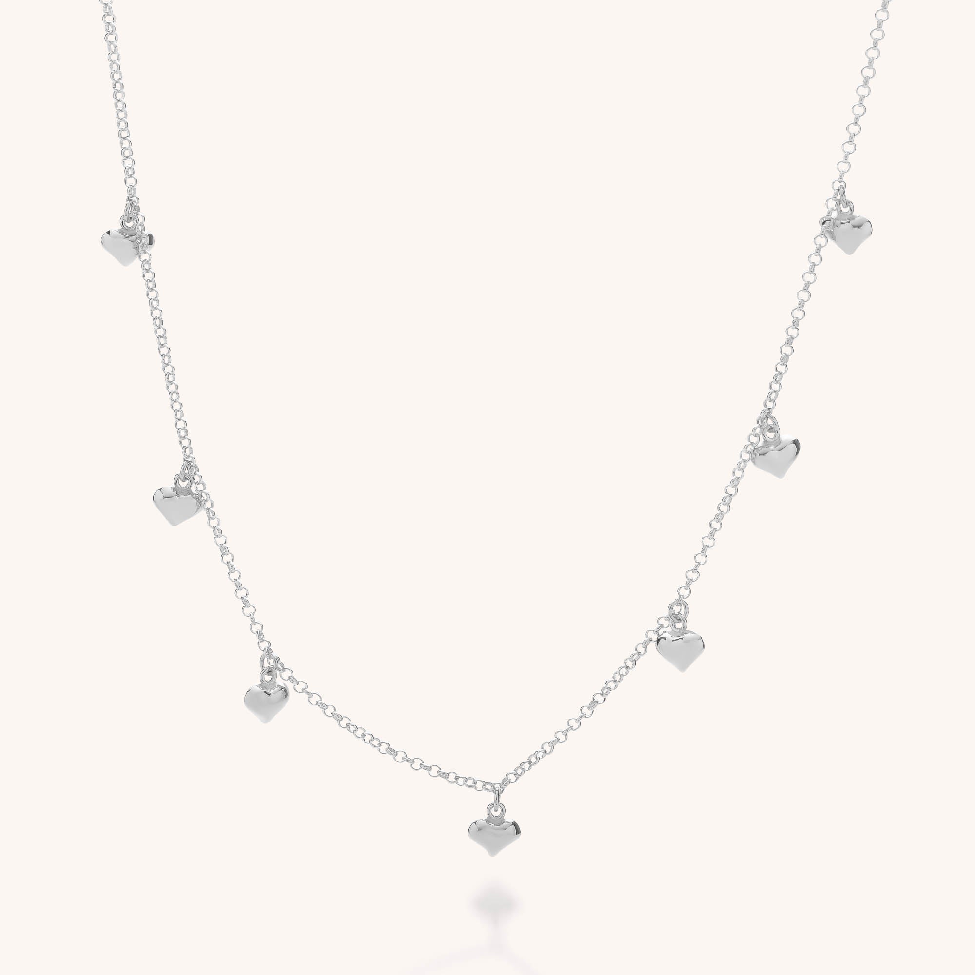 The Floating Heart Charm Necklace, crafted from eco sterling silver, features small, evenly spaced floating heart charms along the chain and is shown against a light, neutral background.