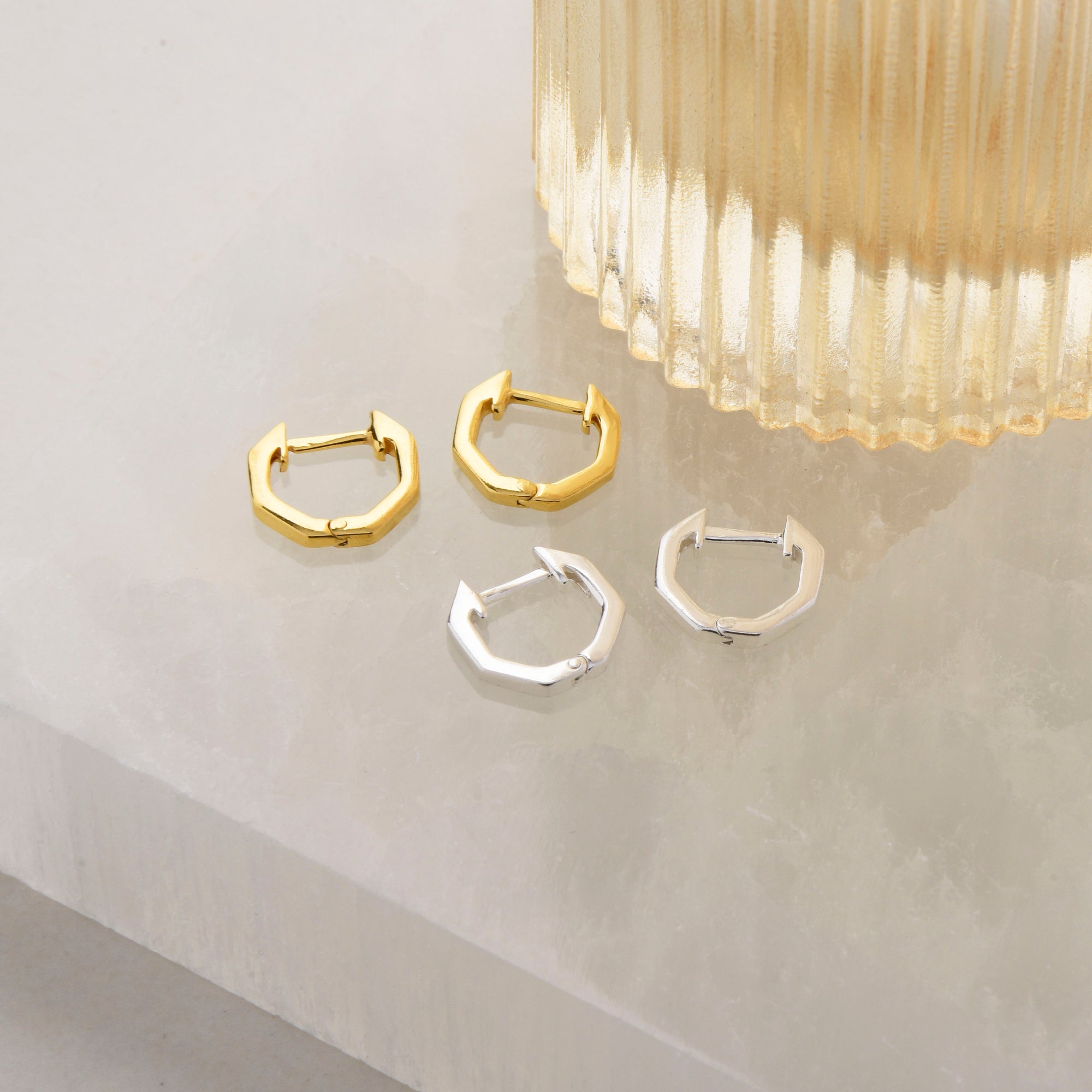 hexagon shaped ear hoops in silver and gold next to a vase