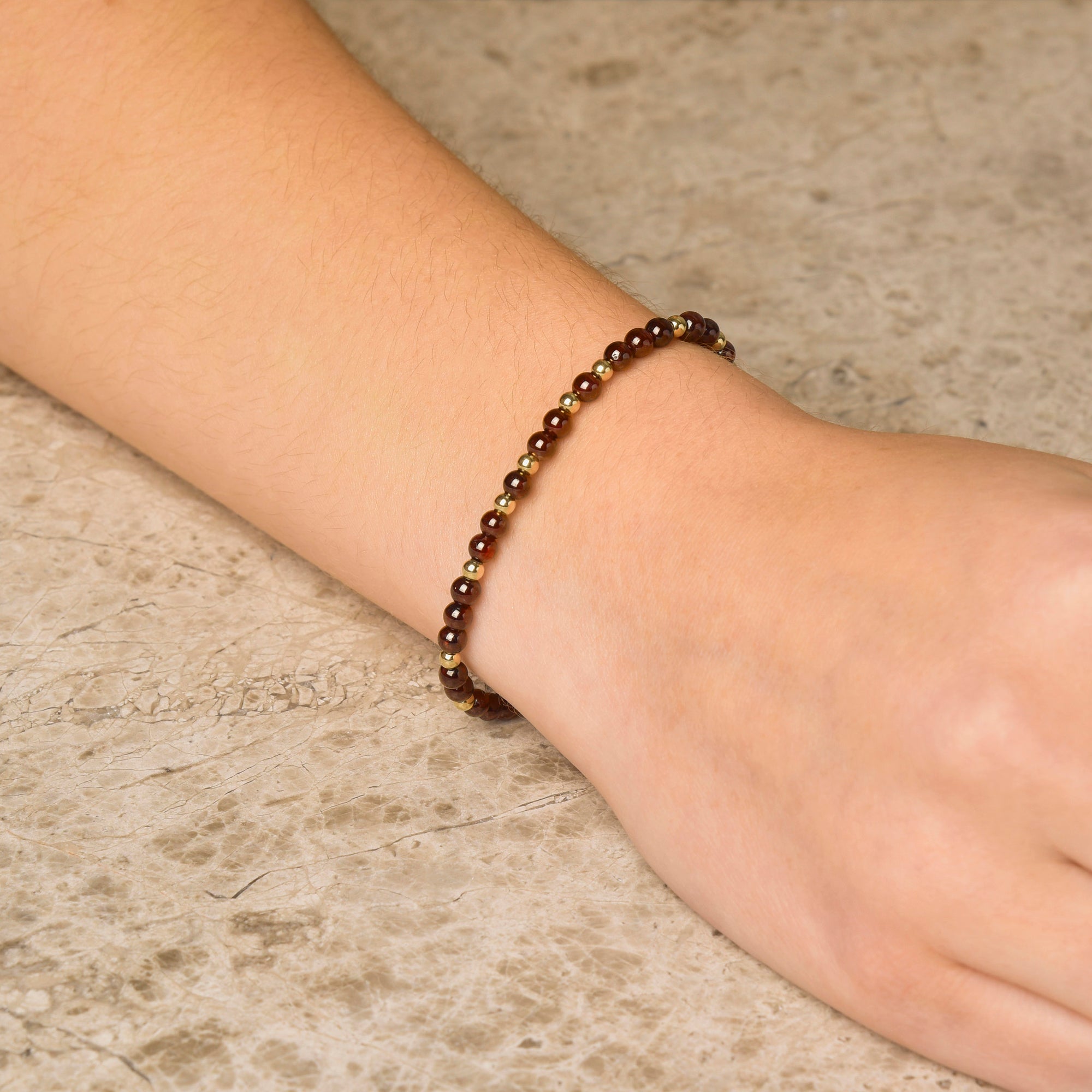 A close-up of a wrist wearing the Jewel Bead Bracelet, featuring small polished brown natural gemstone beads, resting on a light stone surface.