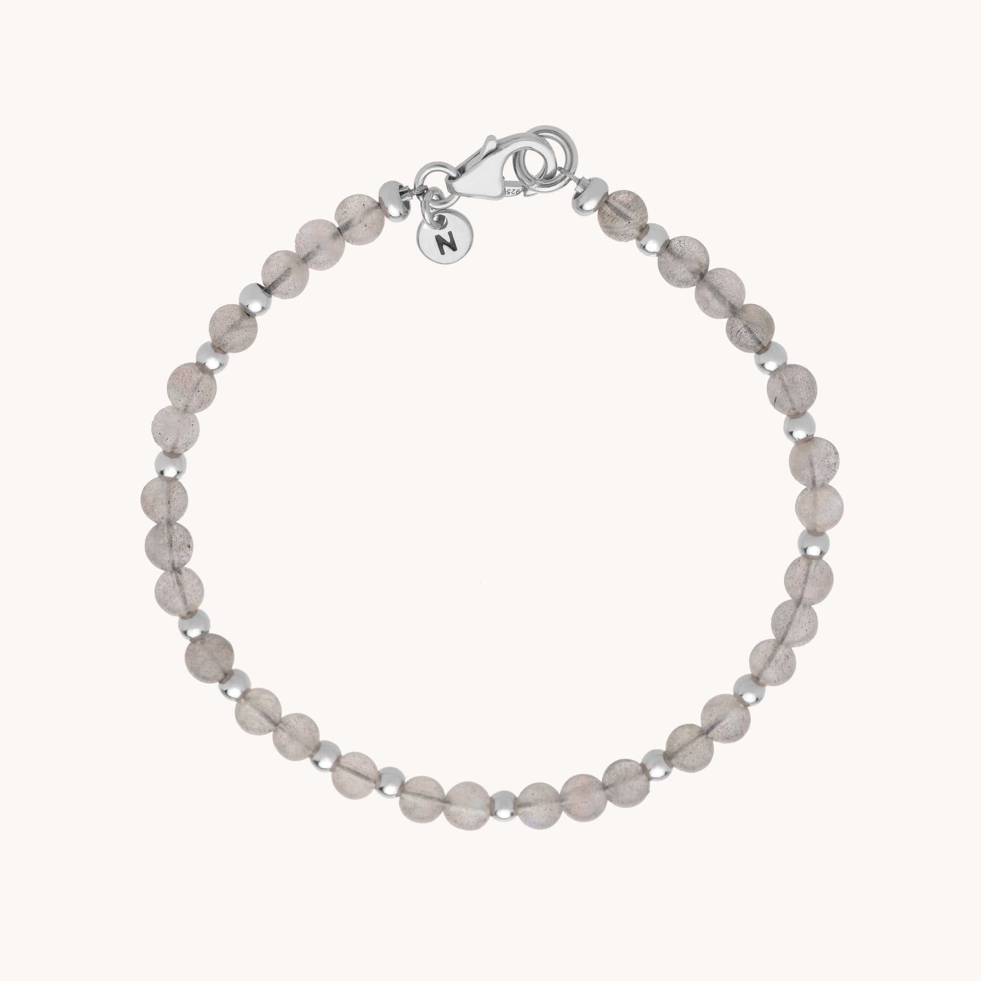 The Jewel Bead Bracelet highlights round, translucent gray gemstones and eco-silver sterling silver spacers, finished with a silver clasp and a small round charm near the closure.