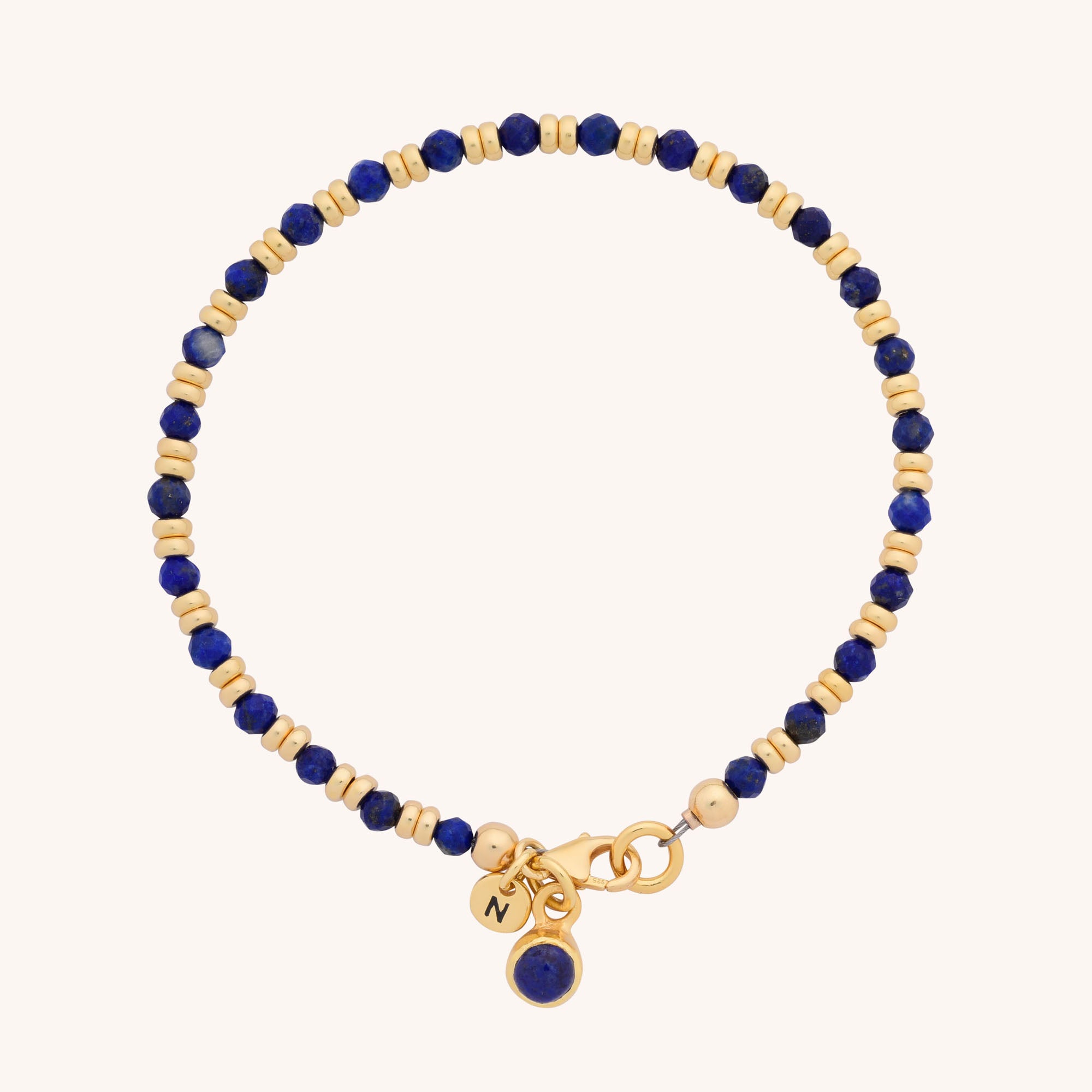 The Linear Birthstone Bracelet - September features alternating small gold and deep blue beads, two gold charms, and a blue gemstone charm near the clasp, elegantly displayed on a light background.