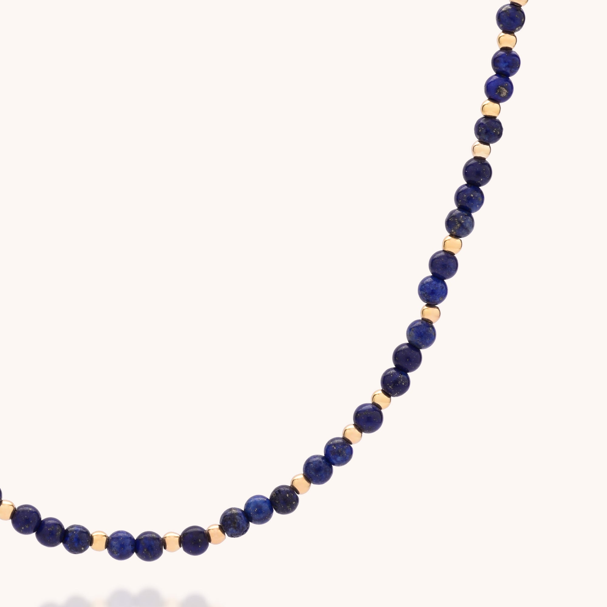 A close-up of the Jewel Bead Birthstone Necklace - September: a handcrafted UK piece featuring alternating deep blue lapis lazuli and small gold round beads, displayed against a plain light background.