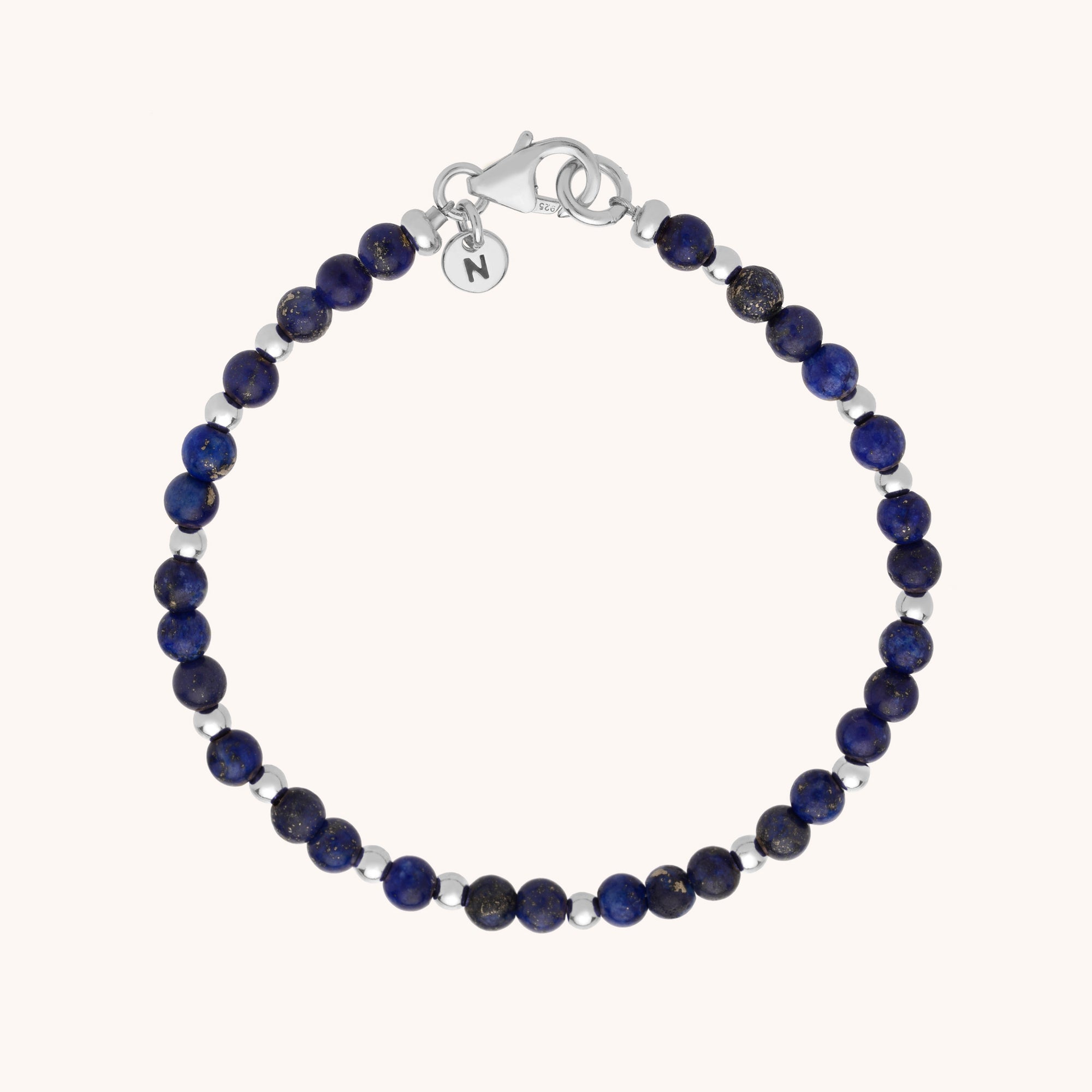 The Jewel Bead Bracelet features round dark blue natural gemstones, small eco-silver sterling silver beads, a silver lobster clasp, and a round charm engraved with the letter N, shown on a light background.