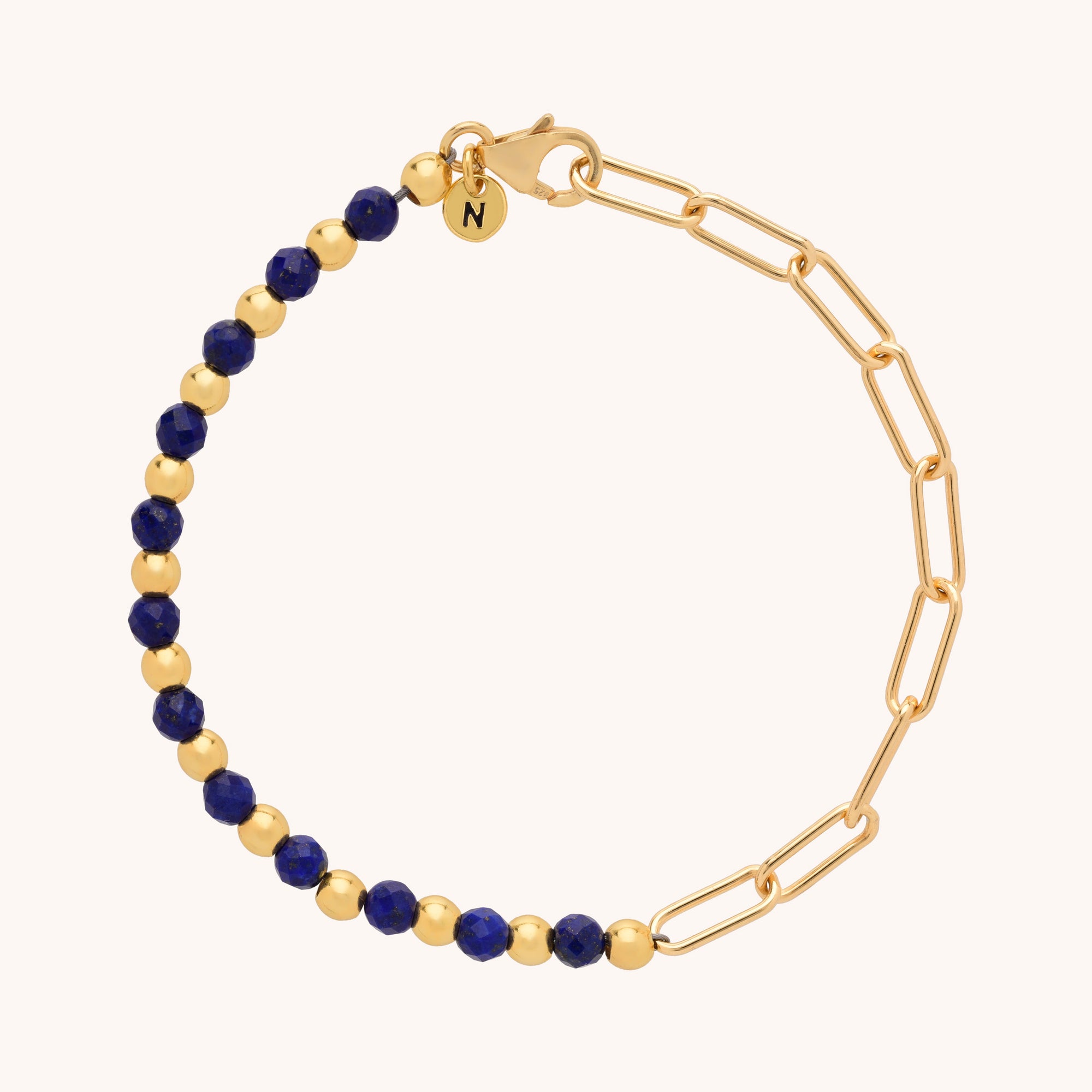 The Gem Shine Bracelet features alternating gold and dark blue gemstone beads on one side, elongated gold chain links on the other, and a round charm engraved with N near the clasp.