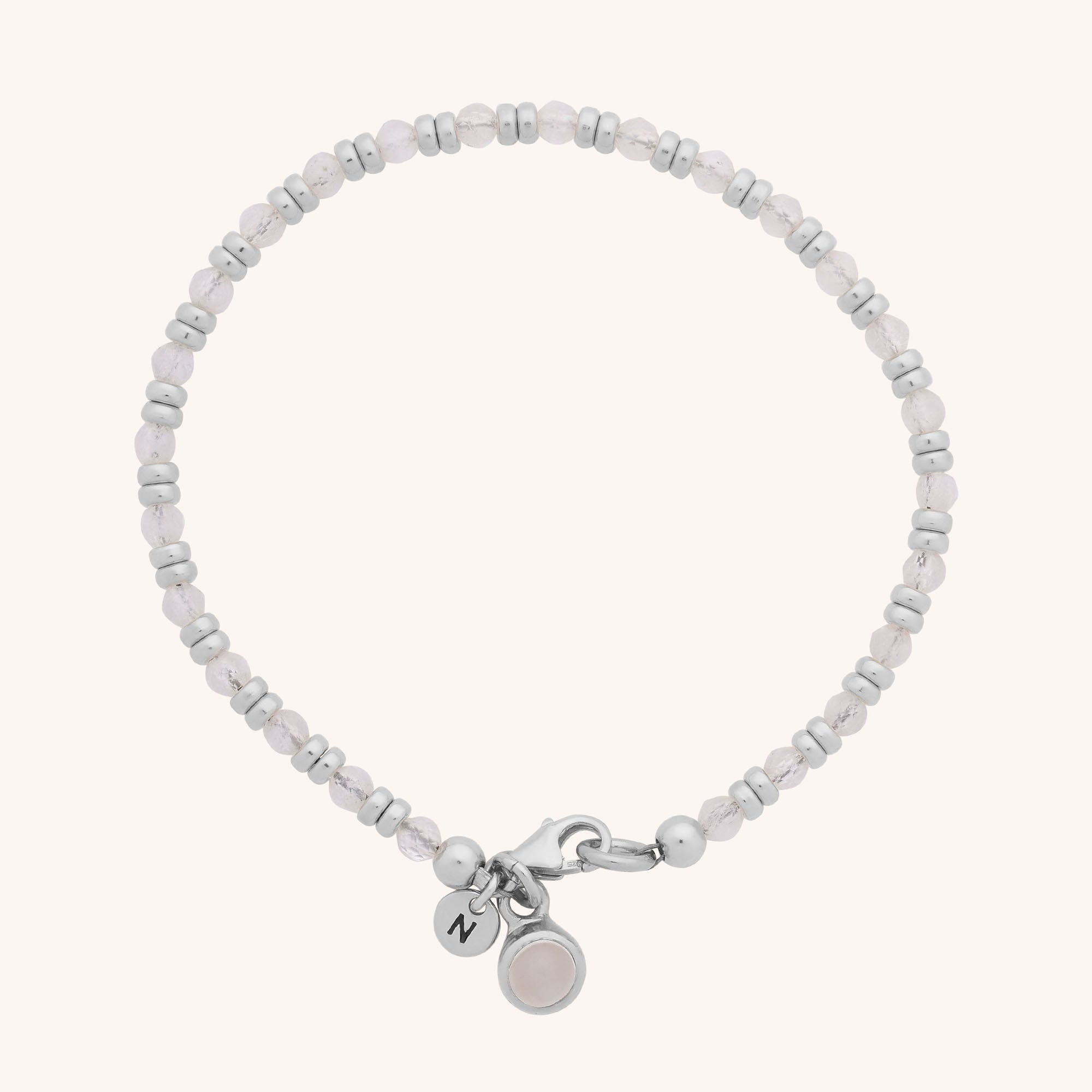 The Linear Birthstone Bracelet features alternating silver and light pink beads, a small silver N-engraved charm, and a round light pink stone charm—ideal for gemstone jewellery lovers.