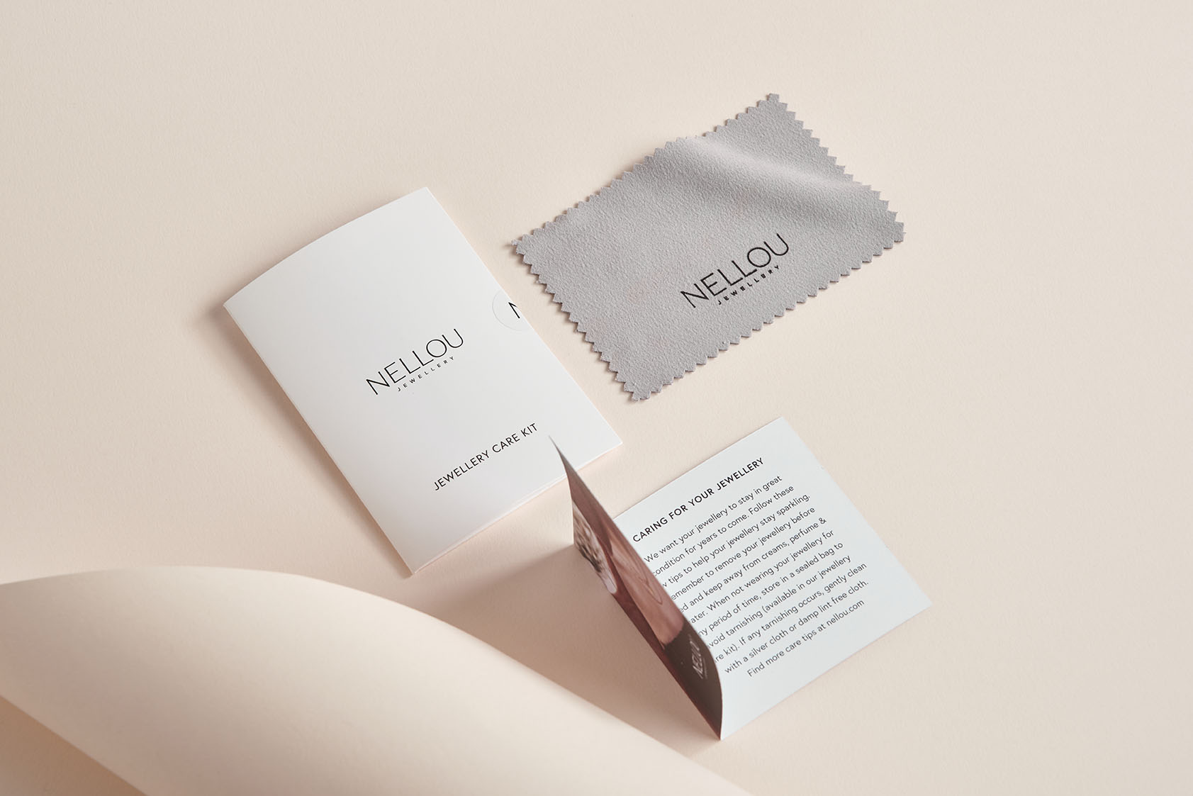 A jewelry care kit including a gray cleaning cloth, a folded instruction card, and a booklet, all branded with NELLOU, displayed on a light beige surface.