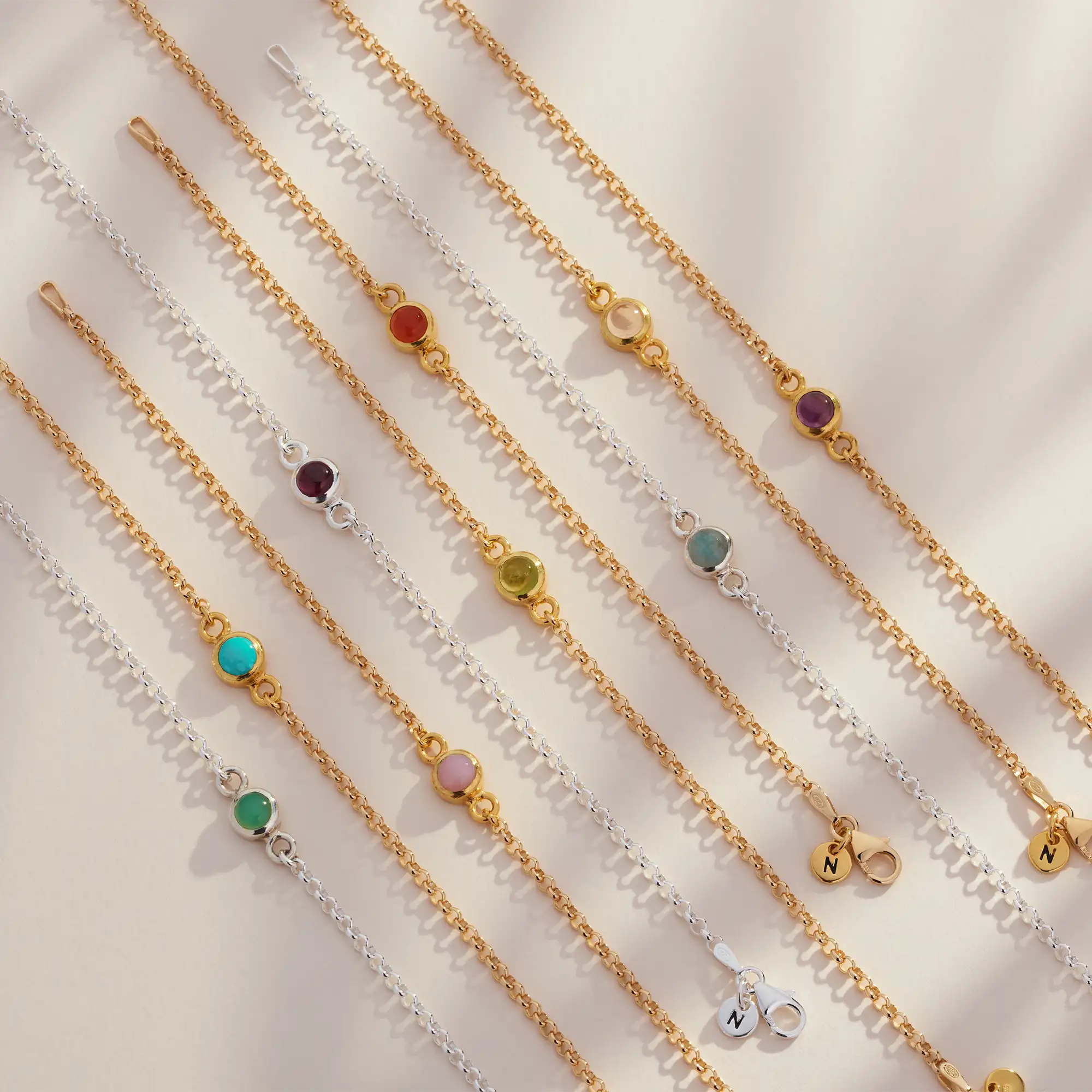 The Birthstone Gem Dot Bracelet - December, featuring a turquoise gemstone, is arranged diagonally on a light background with soft shadows; some bracelets also include small round charm pendants.