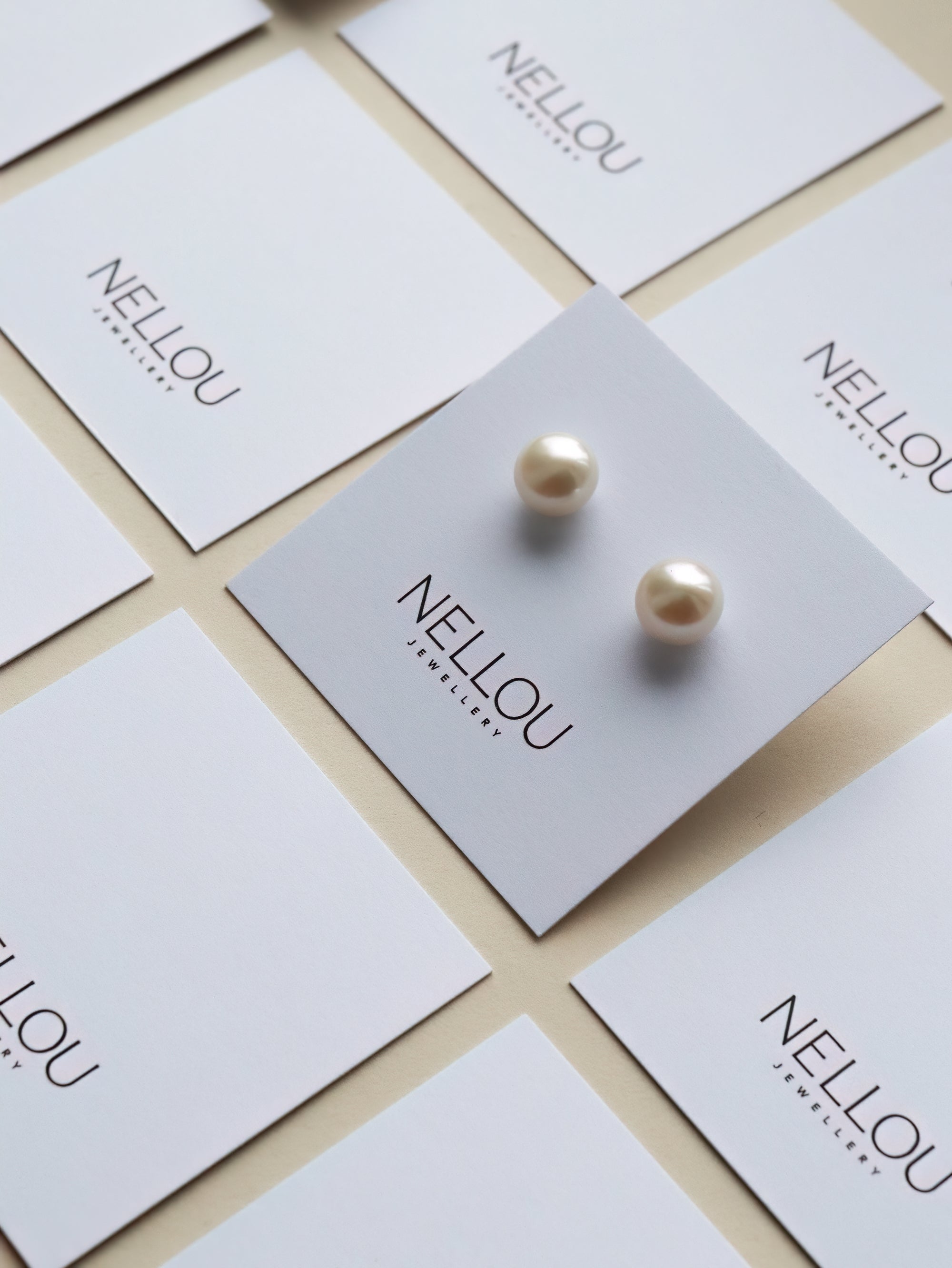 Several white cards with the text NELLOU JEWELLERY are arranged in a grid pattern; one card displays a pair of pearl earrings.