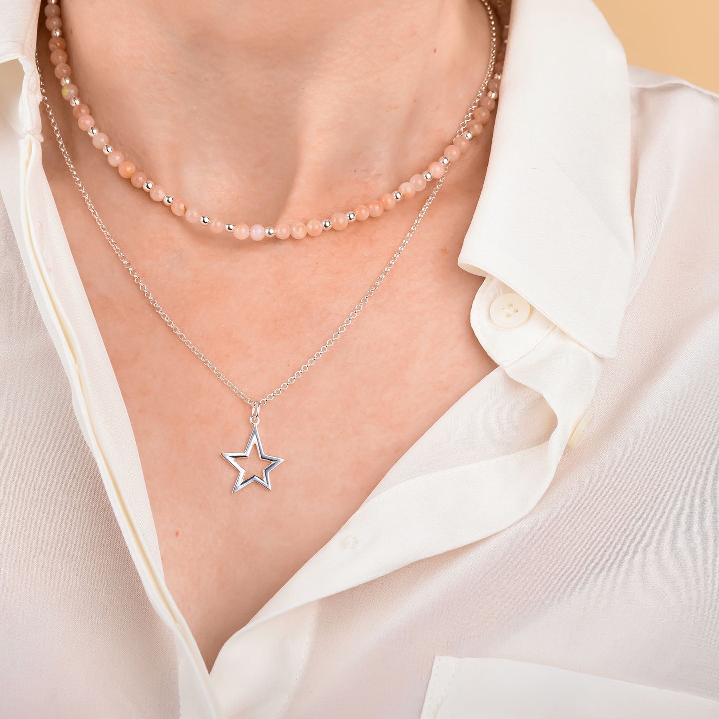 A person in a white button-up shirt showcases two necklaces: a beaded choker and the Northern Star Necklace, a longer sterling silver chain featuring a celestial star charm.