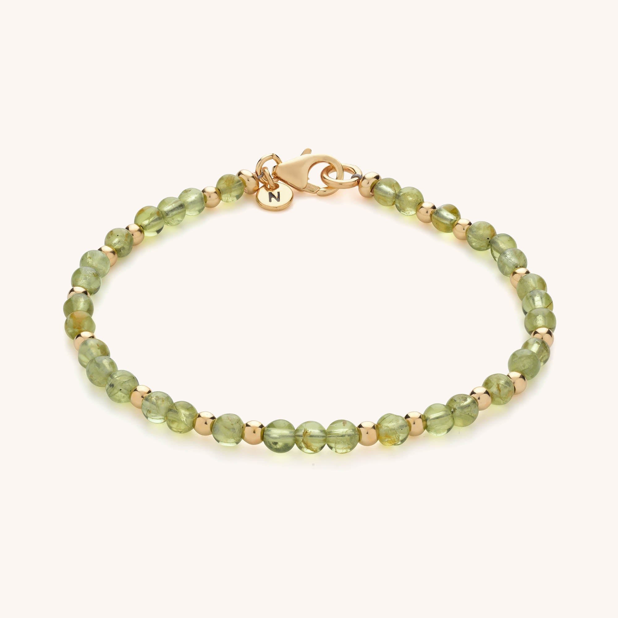 Introducing the Jewel Bead Birthstone Bracelet—featuring small round green beads, gold spacers, a gold clasp, and a round N-engraved charm. A perfect handmade jewellery gift for those who love personalized style.