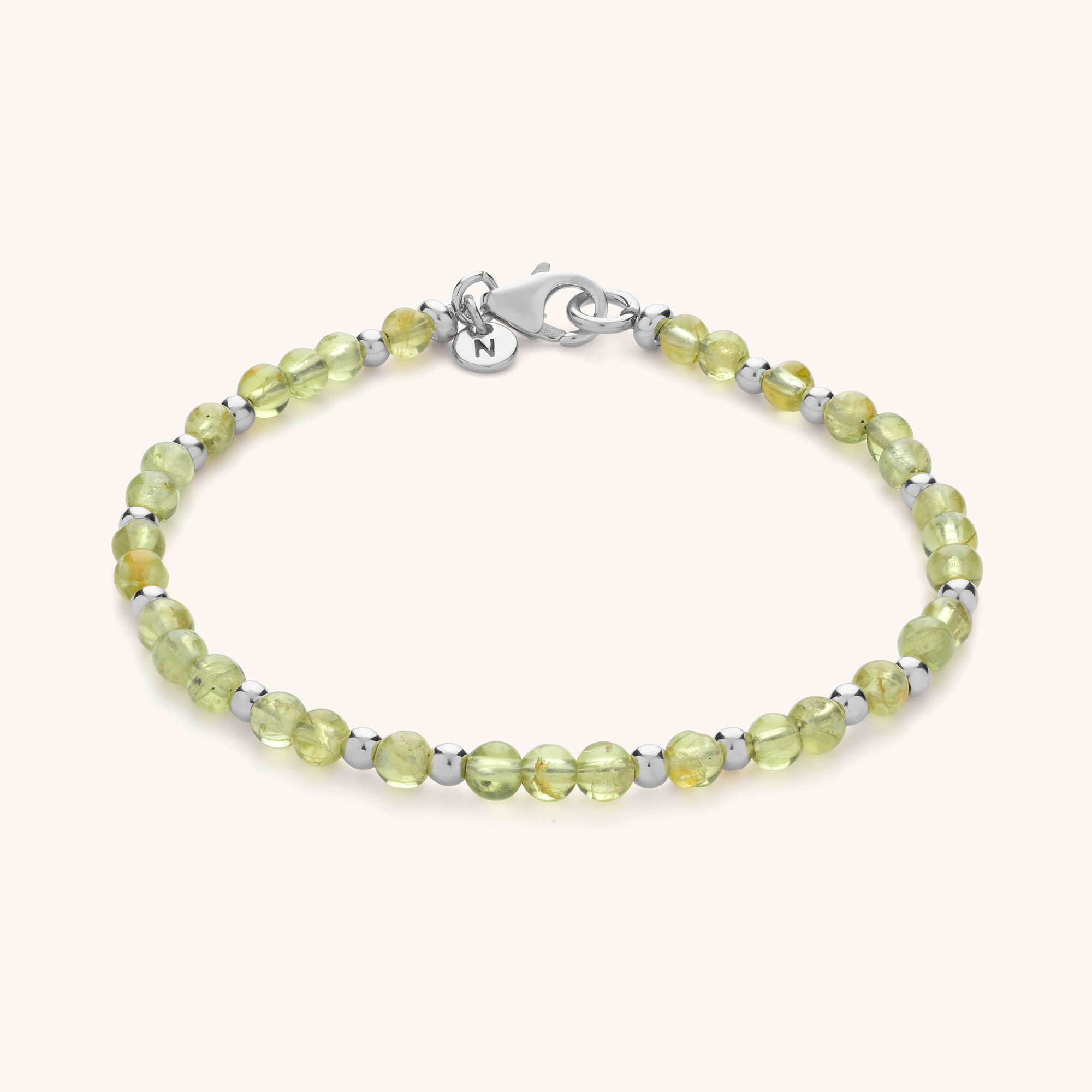 The Jewel Bead Birthstone Bracelet features light green round beads with small silver accents, finished with a silver lobster clasp and a round charm engraved with the letter N—a perfect piece of handmade jewellery.