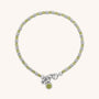 The Linear Birthstone Bracelet is a delicate piece with alternating silver and light green beads, a silver clasp, and two charms—one engraved with “N” and one featuring a green center—ideal for gemstone jewelry lovers.