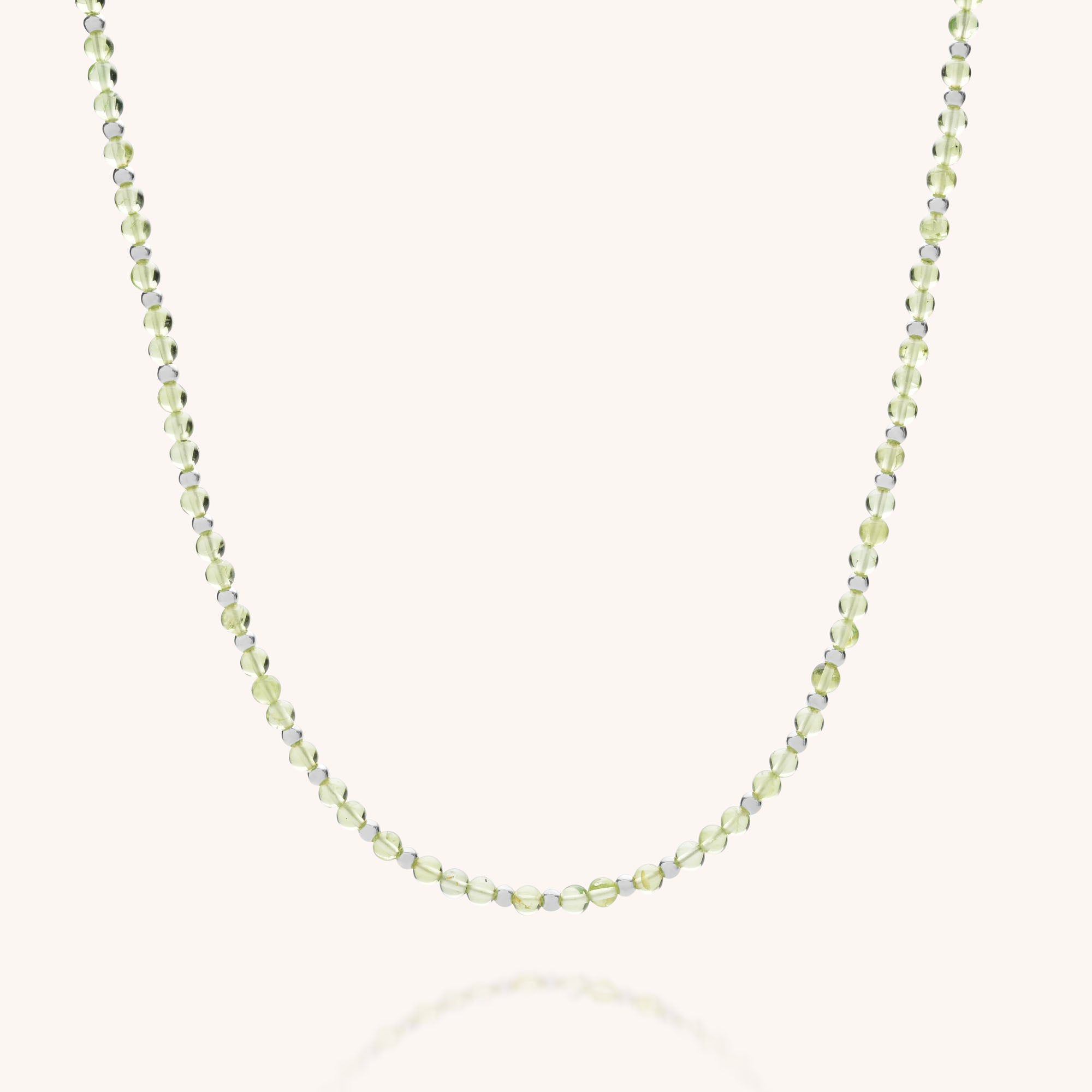 The Jewel Bead Birthstone Necklace - August is a delicate, handmade UK necklace featuring small, translucent green peridot and white beads on a thin string, beautifully displayed against a light background.