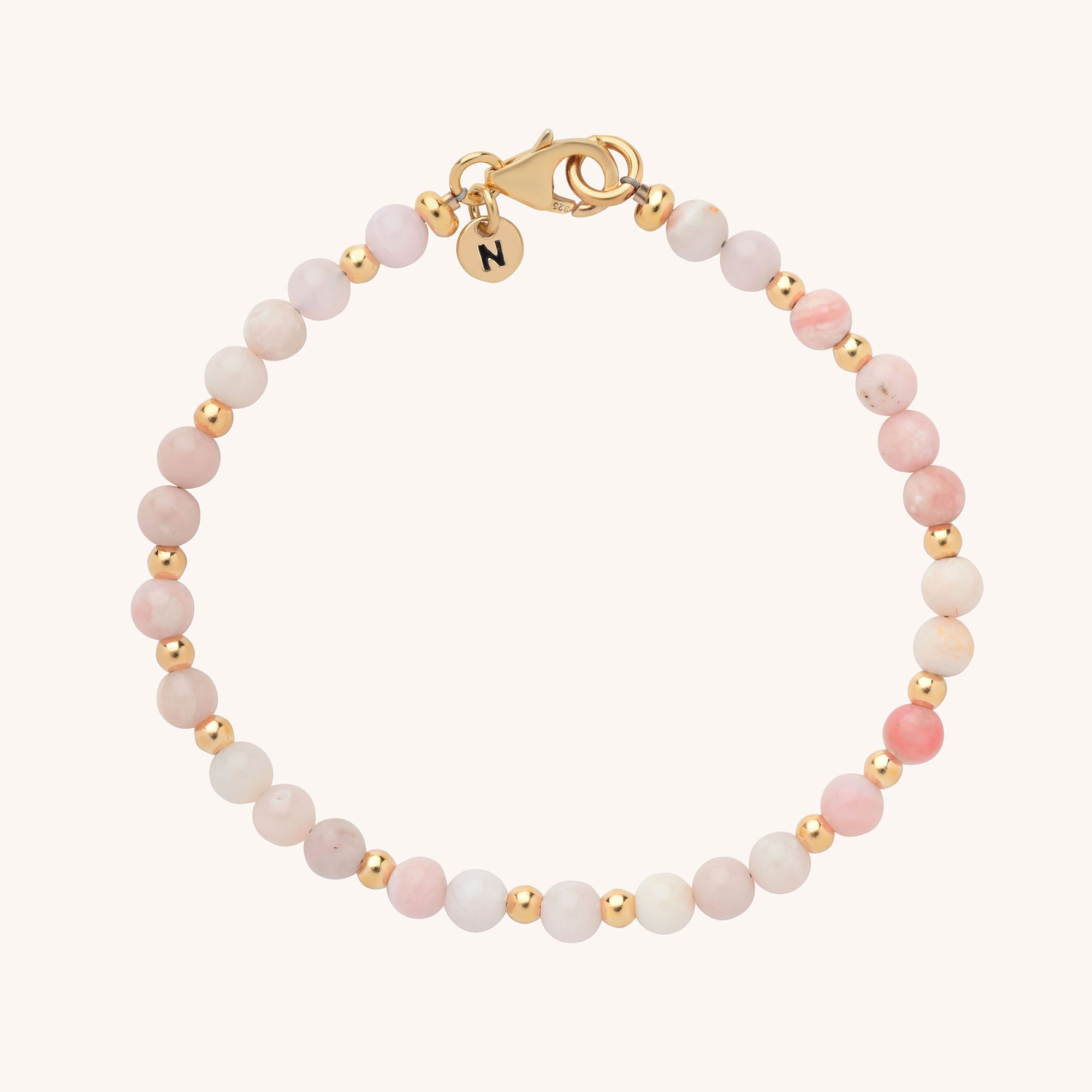 Introducing the Jewel Bead Birthstone Bracelet—handmade with alternating small pink and gold beads, a gold clasp, and a round gold charm engraved with the letter N for a personalized touch.