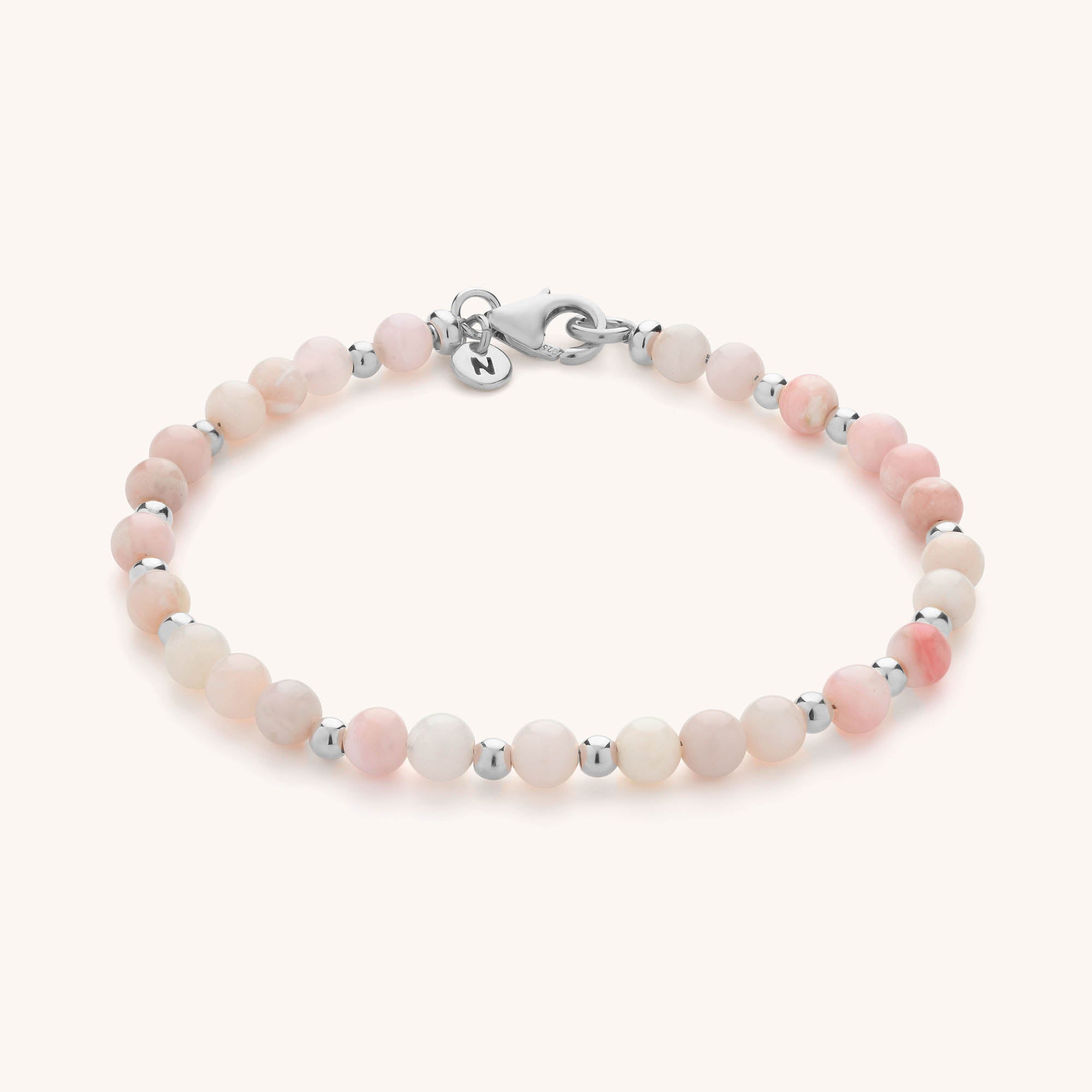 The Jewel Bead Birthstone Bracelet features round, pale pink beads with silver spacers, a silver clasp, and a small round charm engraved with the letter N—making it a beautiful piece of handmade jewellery.