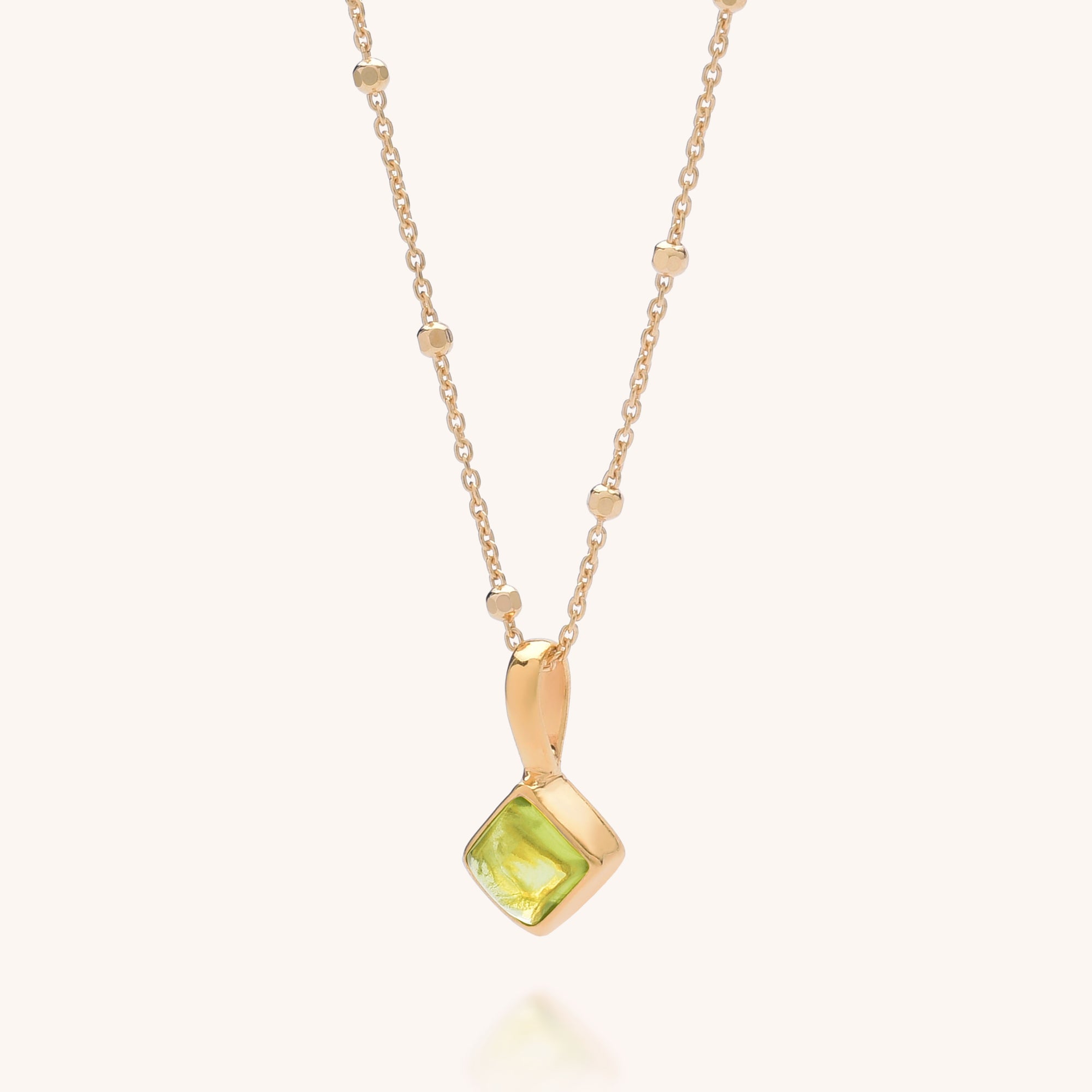 The Diamond Birthstone Necklace August features small gold beads and a square Peridot Gem pendant set in a gold frame, shown on a light background.