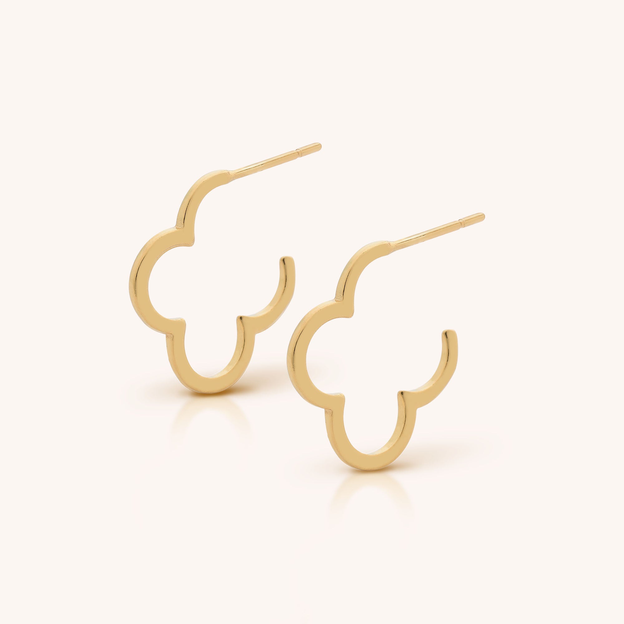 The Clover Hoop Earrings are gold, stylized four-leaf clover-shaped hoops, shown against a simple light background.