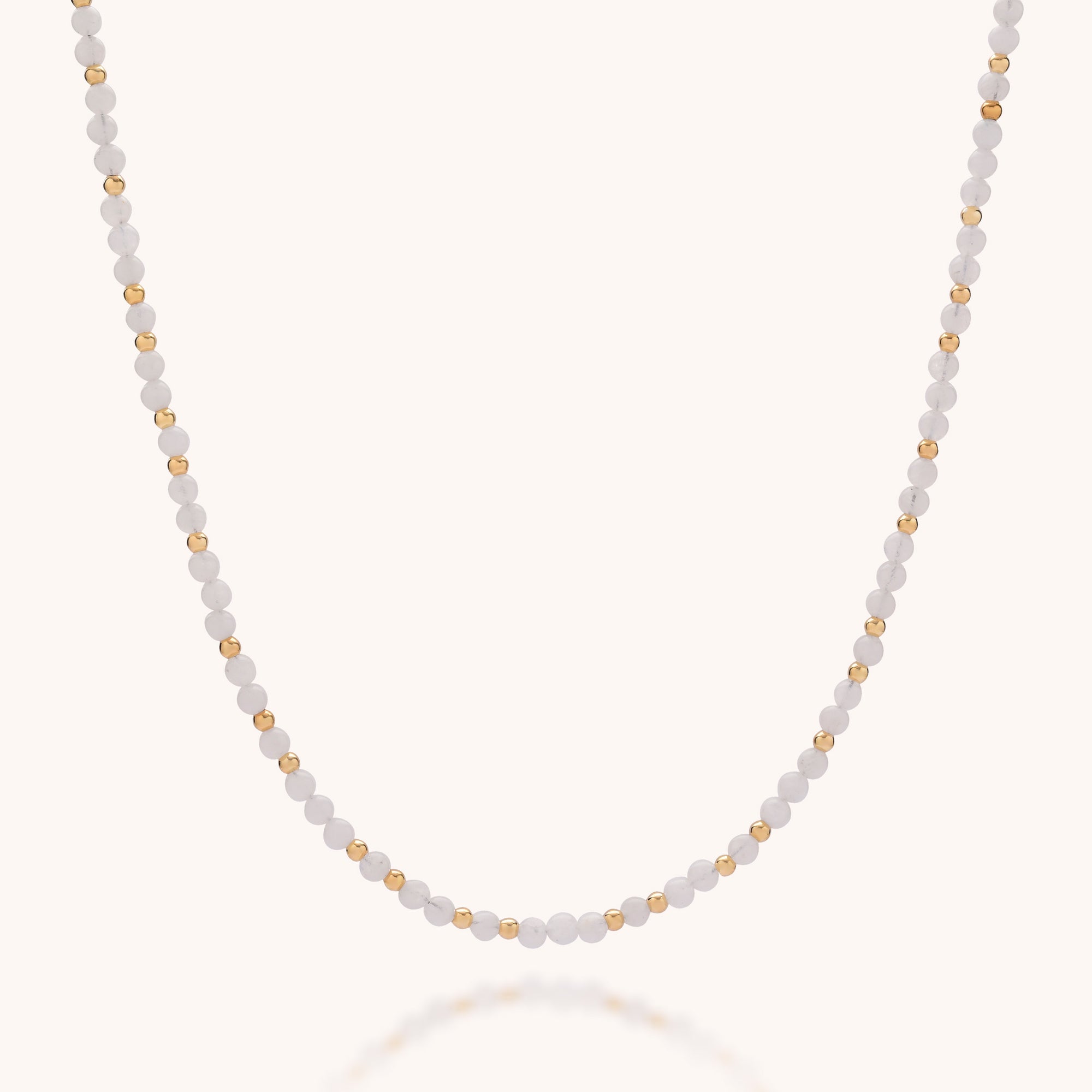 The Jewel Bead Birthstone Necklace - June features alternating small white and gold beads with a shimmering Rainbow Moonstone—June’s birthstone—displayed on a plain, light background and arranged in a gentle curve.