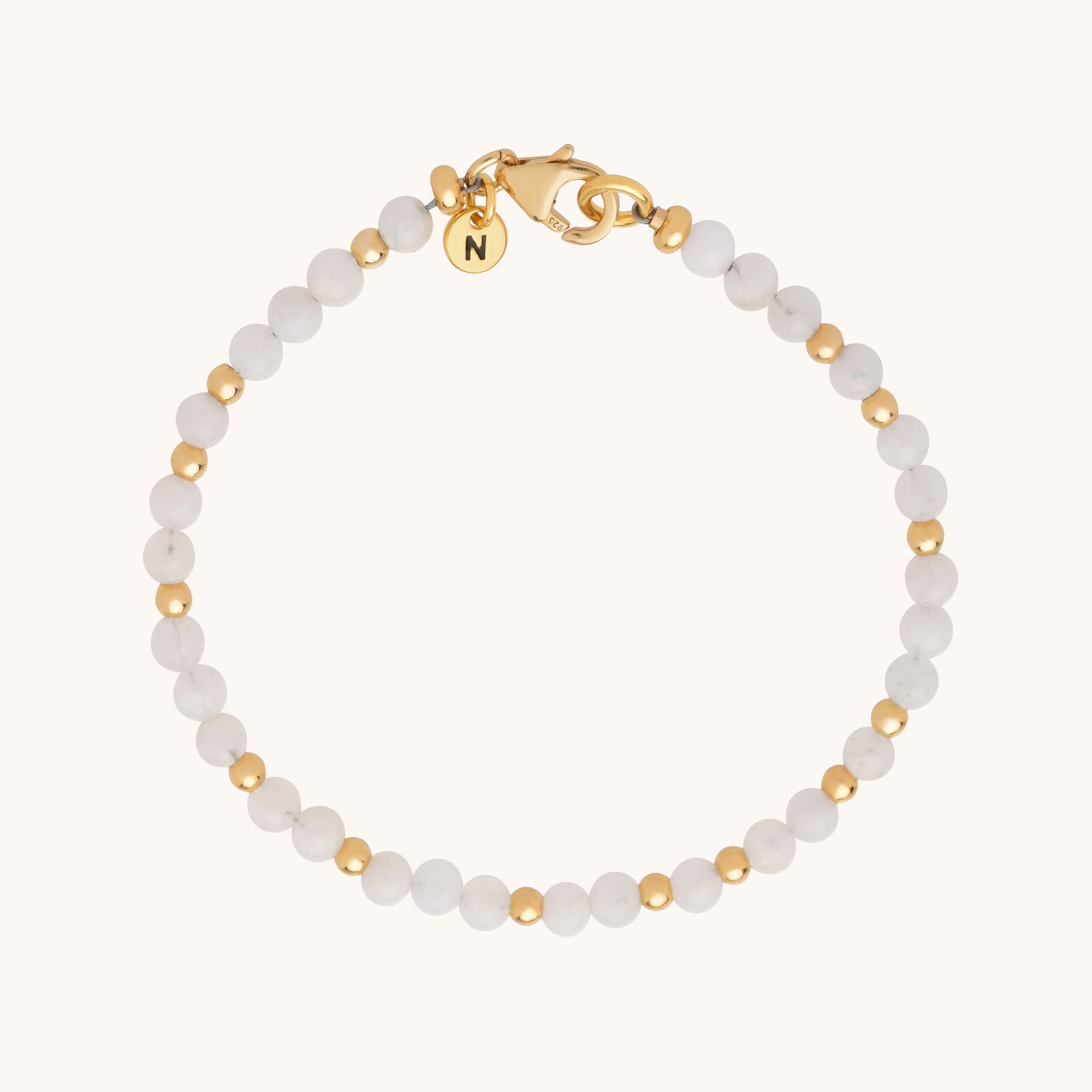 The Jewel Bead Bracelet features alternating small white natural gemstones and gold beads, finished with a gold lobster clasp and a round gold charm engraved with N.