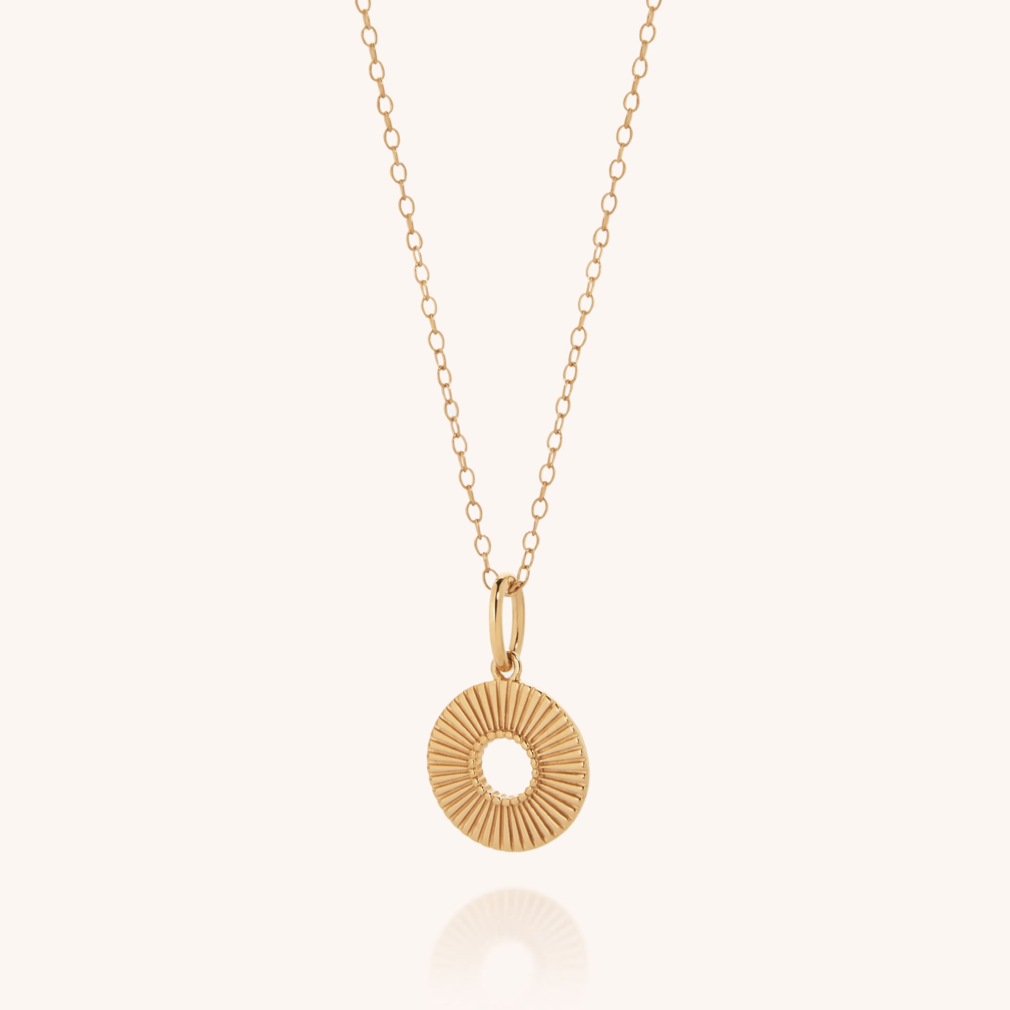 The Solar Circle Necklace features a delicate gold-plated sterling silver chain and a round, sunburst-patterned pendant, beautifully displayed on a simple light background.