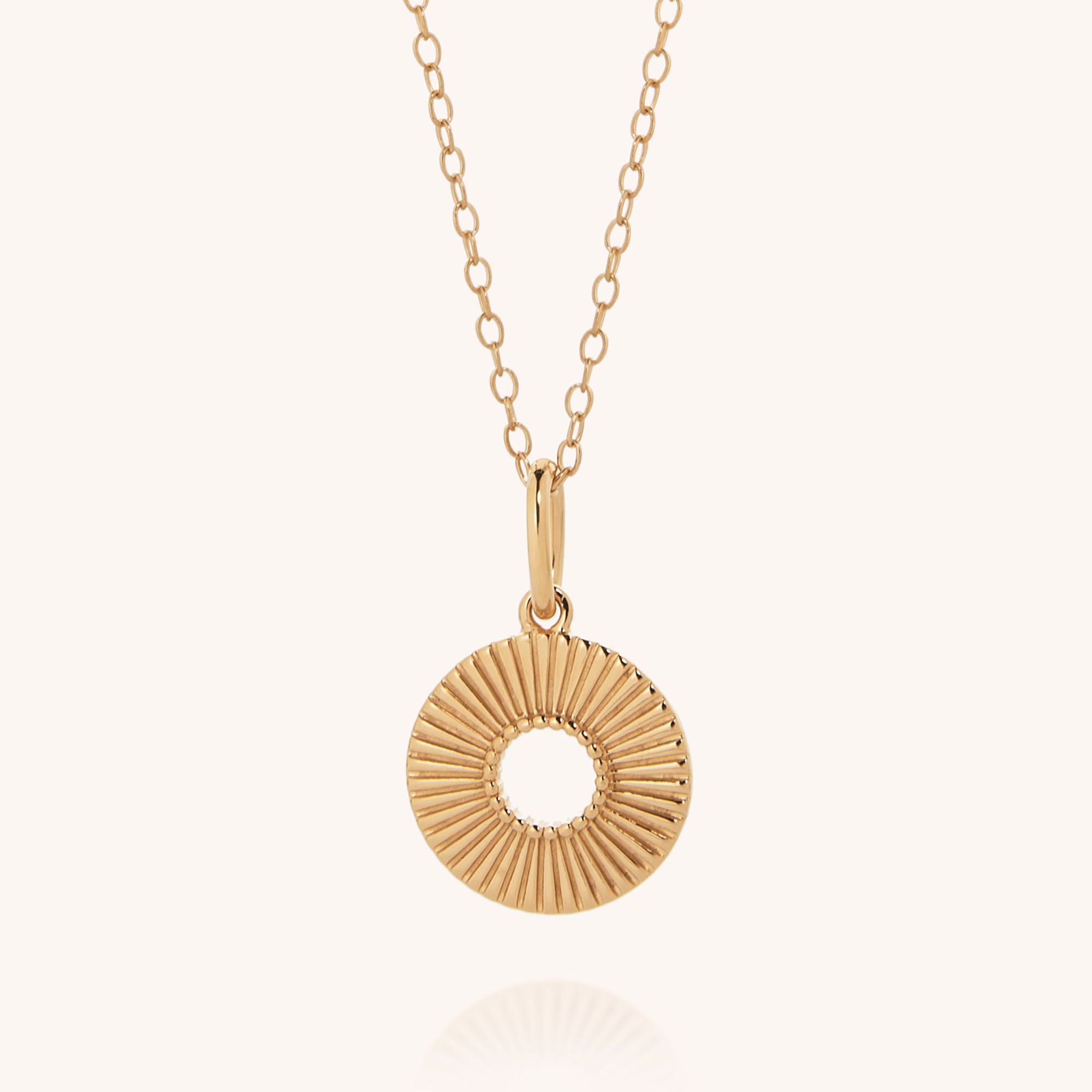 The Solar Circle Necklace is a gold-plated sterling silver necklace with a thin chain and a circular sunburst pendant featuring radiating lines and an open center, shown against a plain, light background.