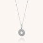 The Solar Circle Necklace in Sterling Silver showcases a thin chain and a round, ridged pendant with a center hole, set against a simple light background.