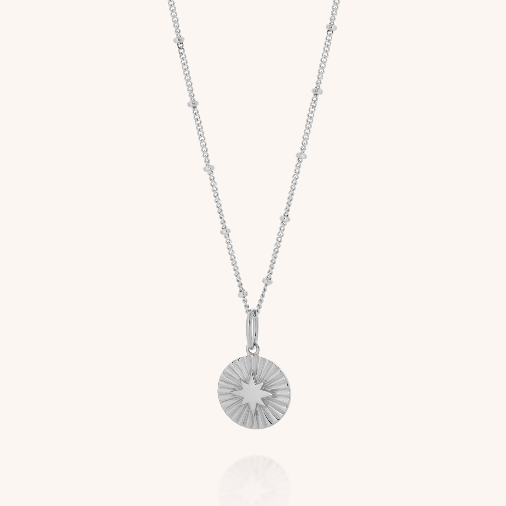 The Shining Star Necklace showcases a beaded sterling silver chain and a round starburst-engraved pendant, offering celestial style.